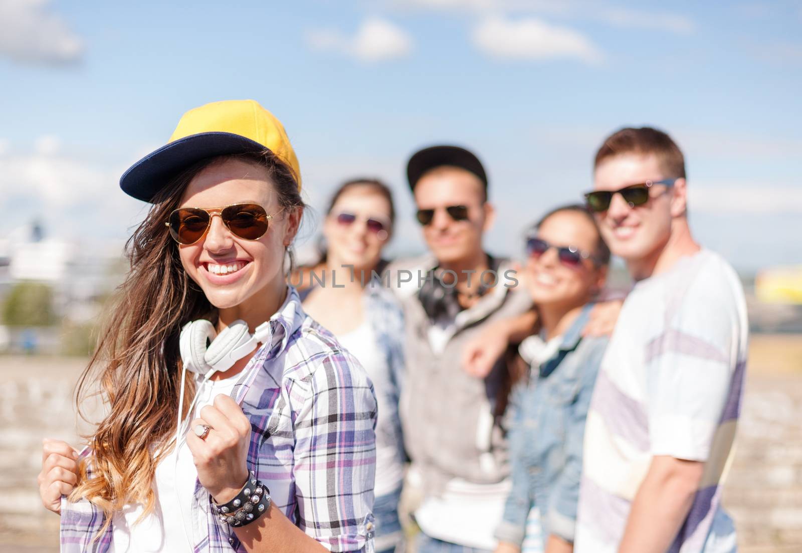 summer holidays and teenage concept - teenage girl in sunglasses, cap and headphones hanging out with friends outside