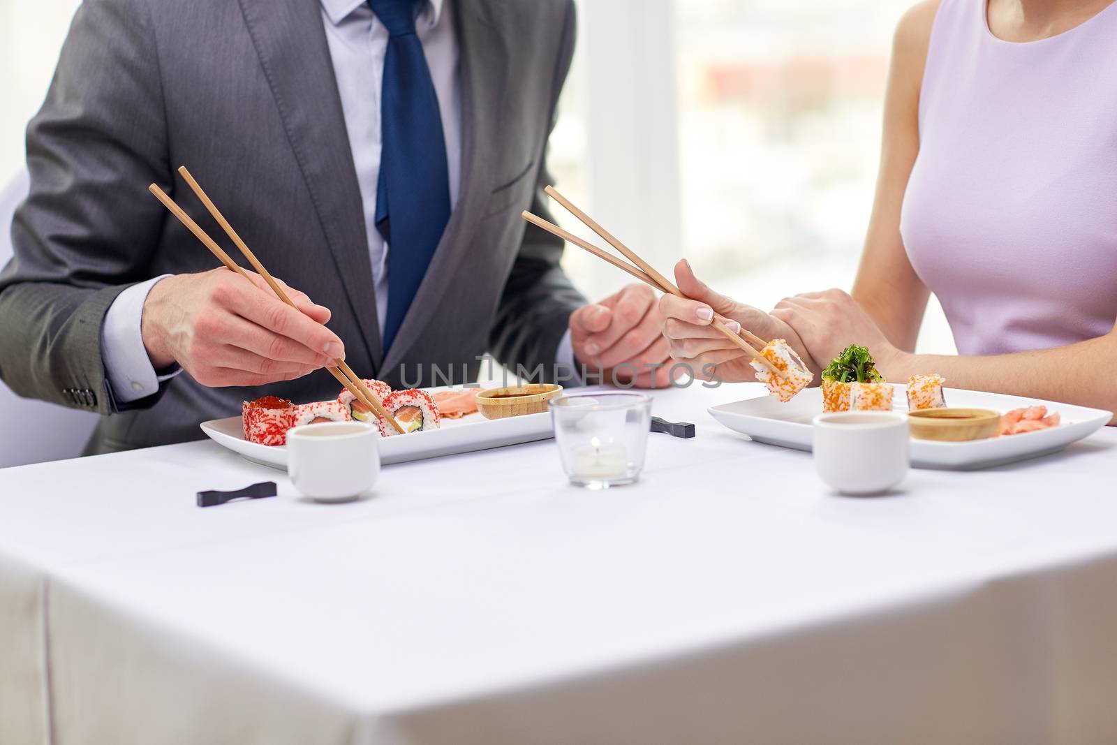 restaurant, food, people, date and holiday concept - close up of couple eating sushi at restaurant