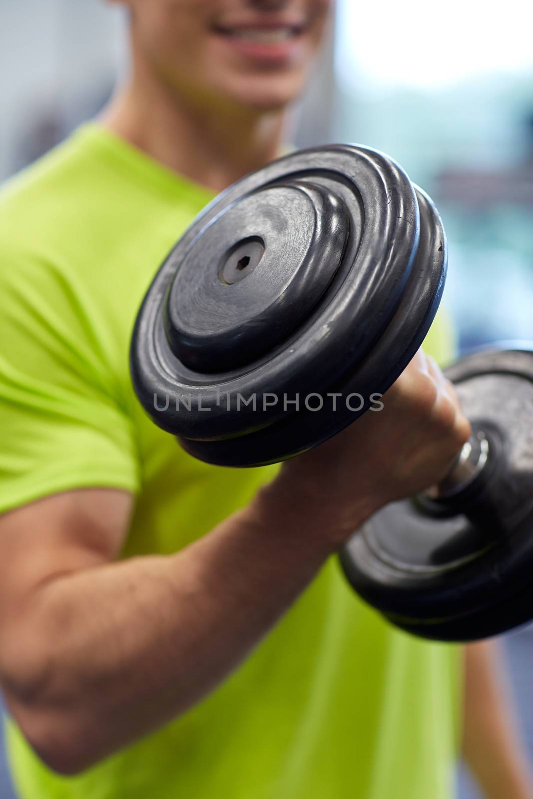 sport, fitness, lifestyle and people concept - close up of smiling man with dumbbell flexing biceps in gym