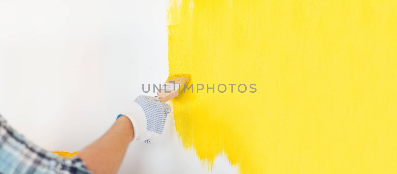 repair and home renovation concept - close up of male hand in gloves painting a wall with yellow paint