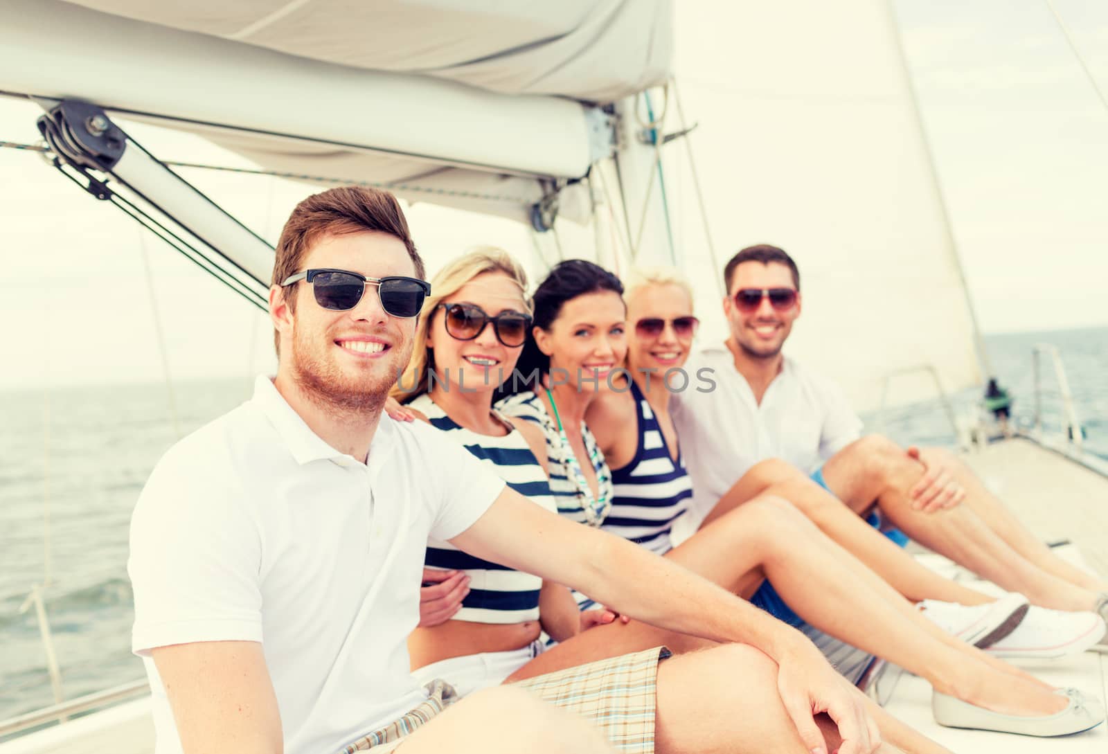 smiling friends sitting on yacht deck by dolgachov