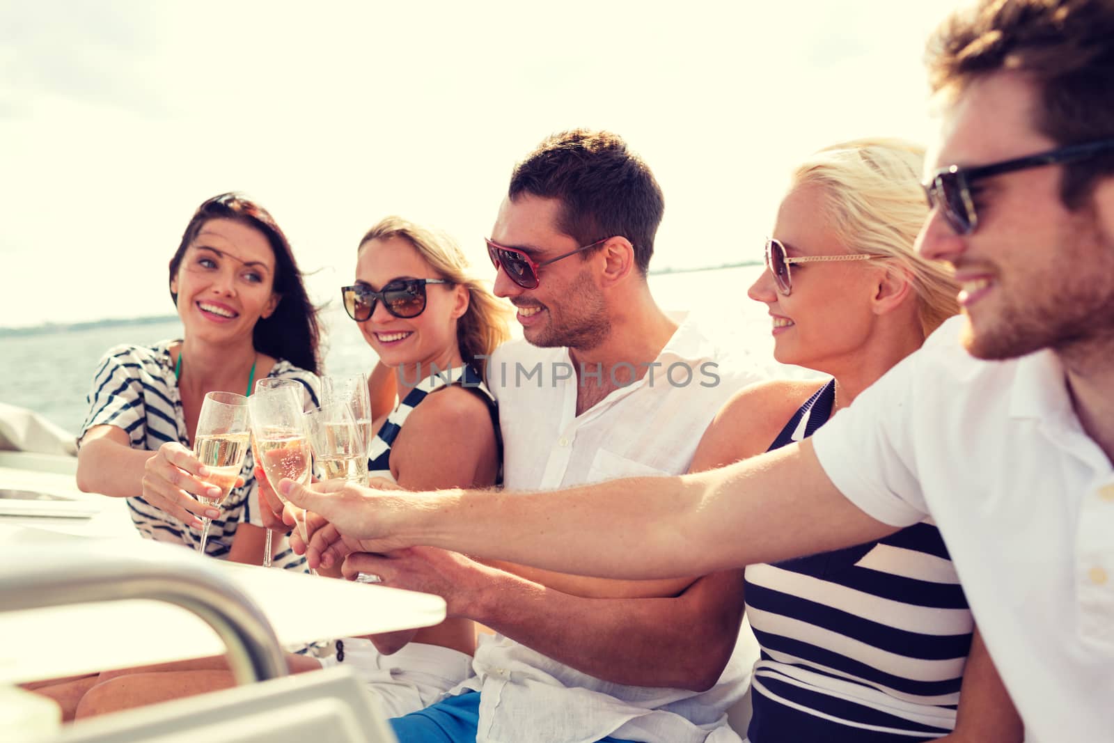 vacation, travel, sea, friendship and people concept - smiling friends with glasses of champagne on yacht