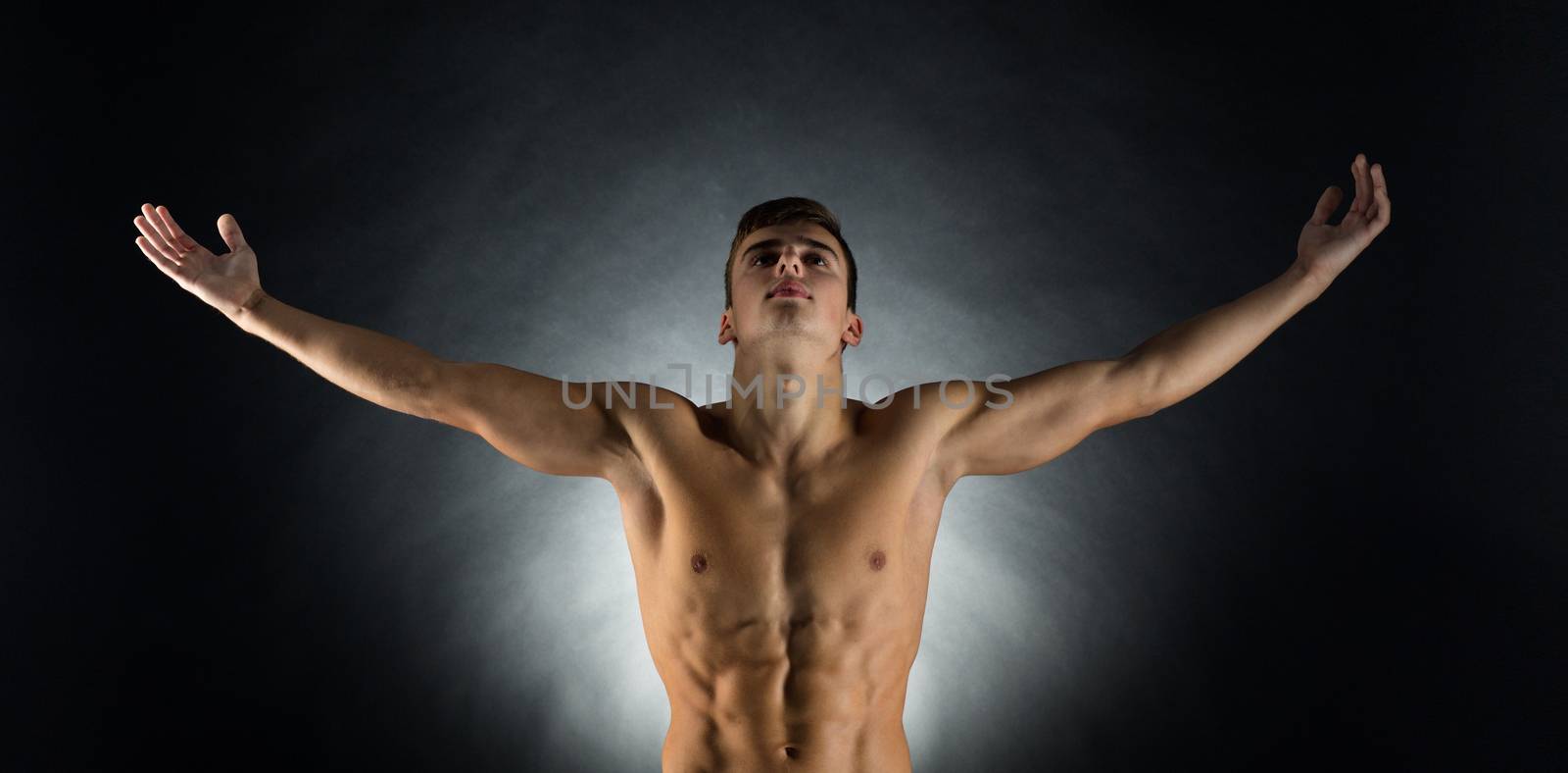 sport, bodybuilding, strength and people concept - young man standing with raised hands over black background