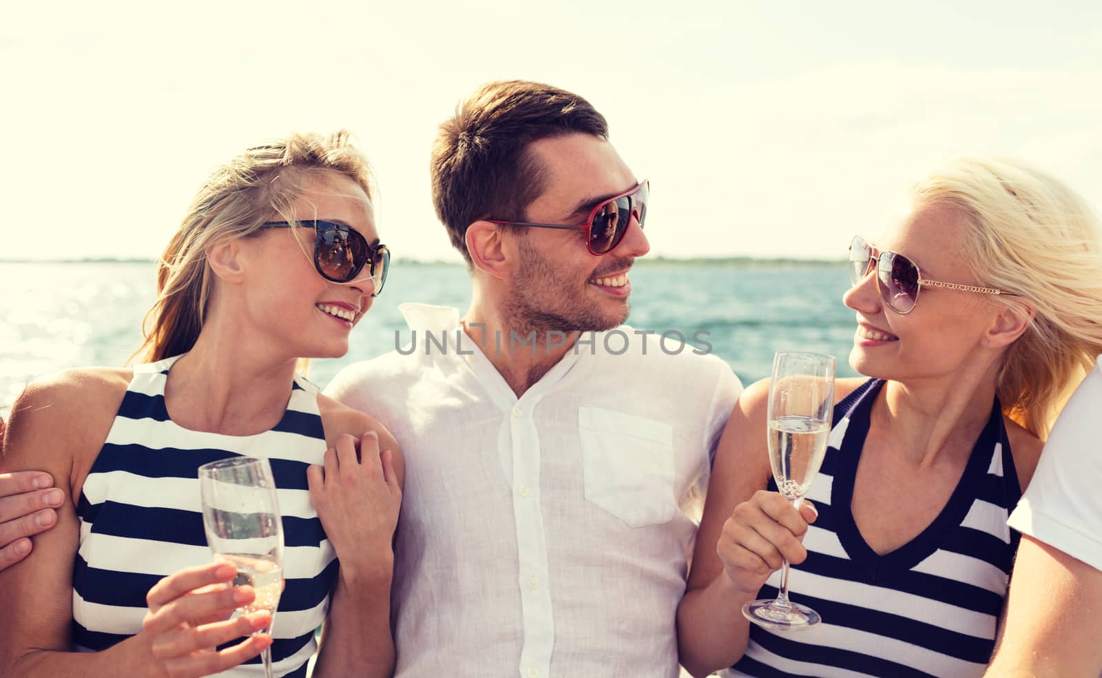 vacation, travel, sea, friendship and people concept - smiling friends with glasses of champagne on yacht