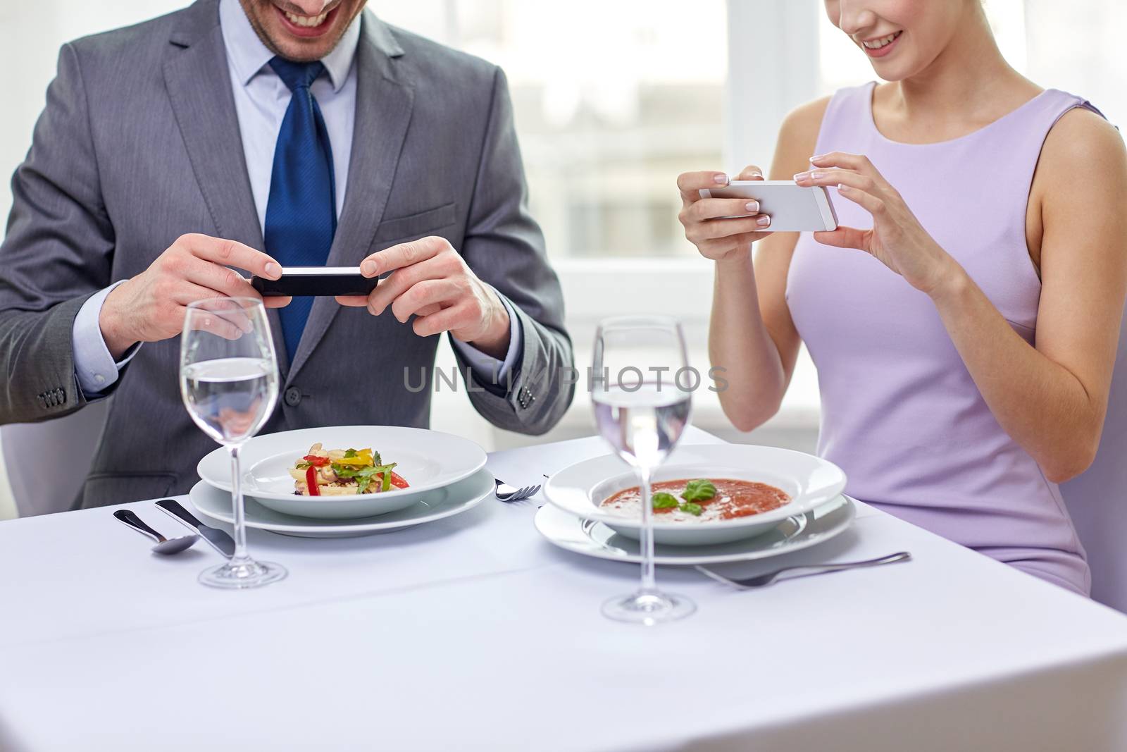 close up of couple with smartphones at restaurant by dolgachov