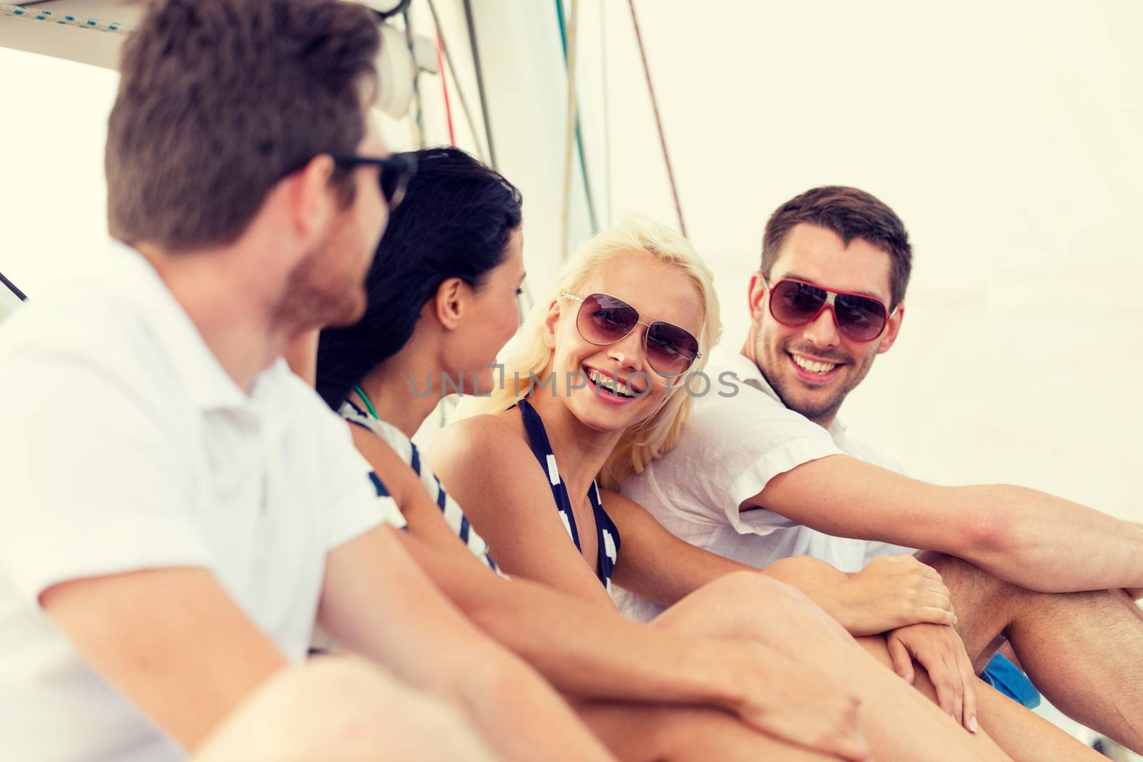 smiling friends sitting on yacht deck by dolgachov