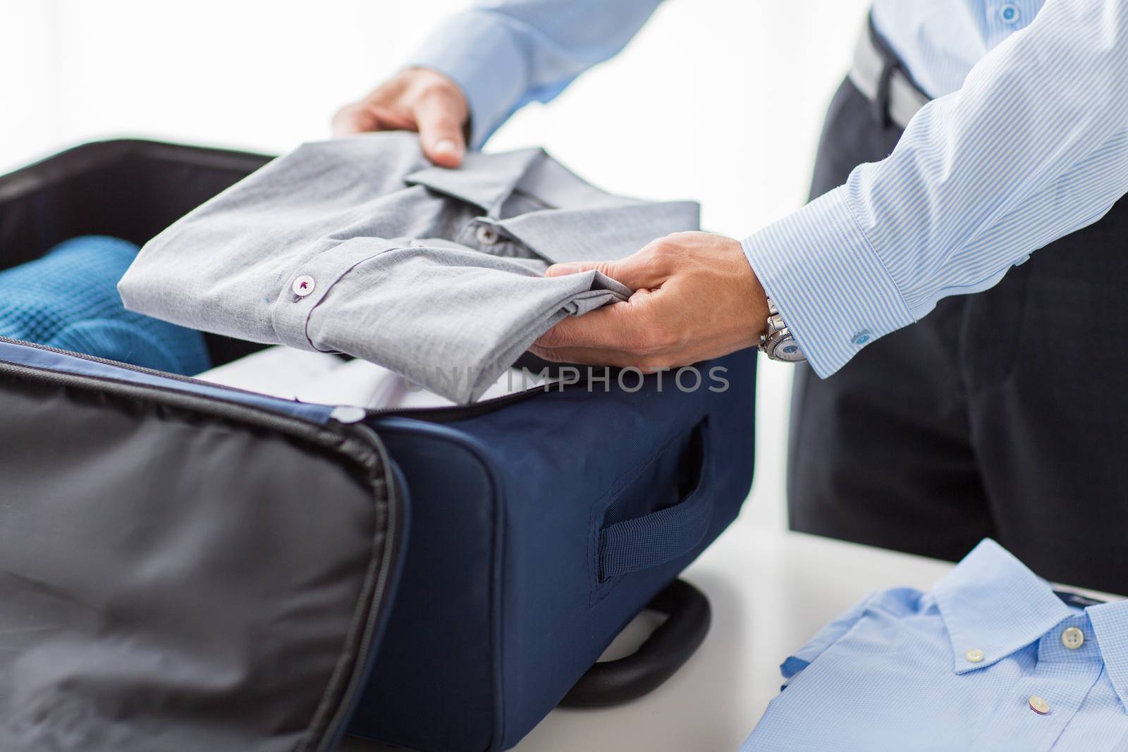 business, trip, luggage and people concept - happy businessman packing clothes into travel bag