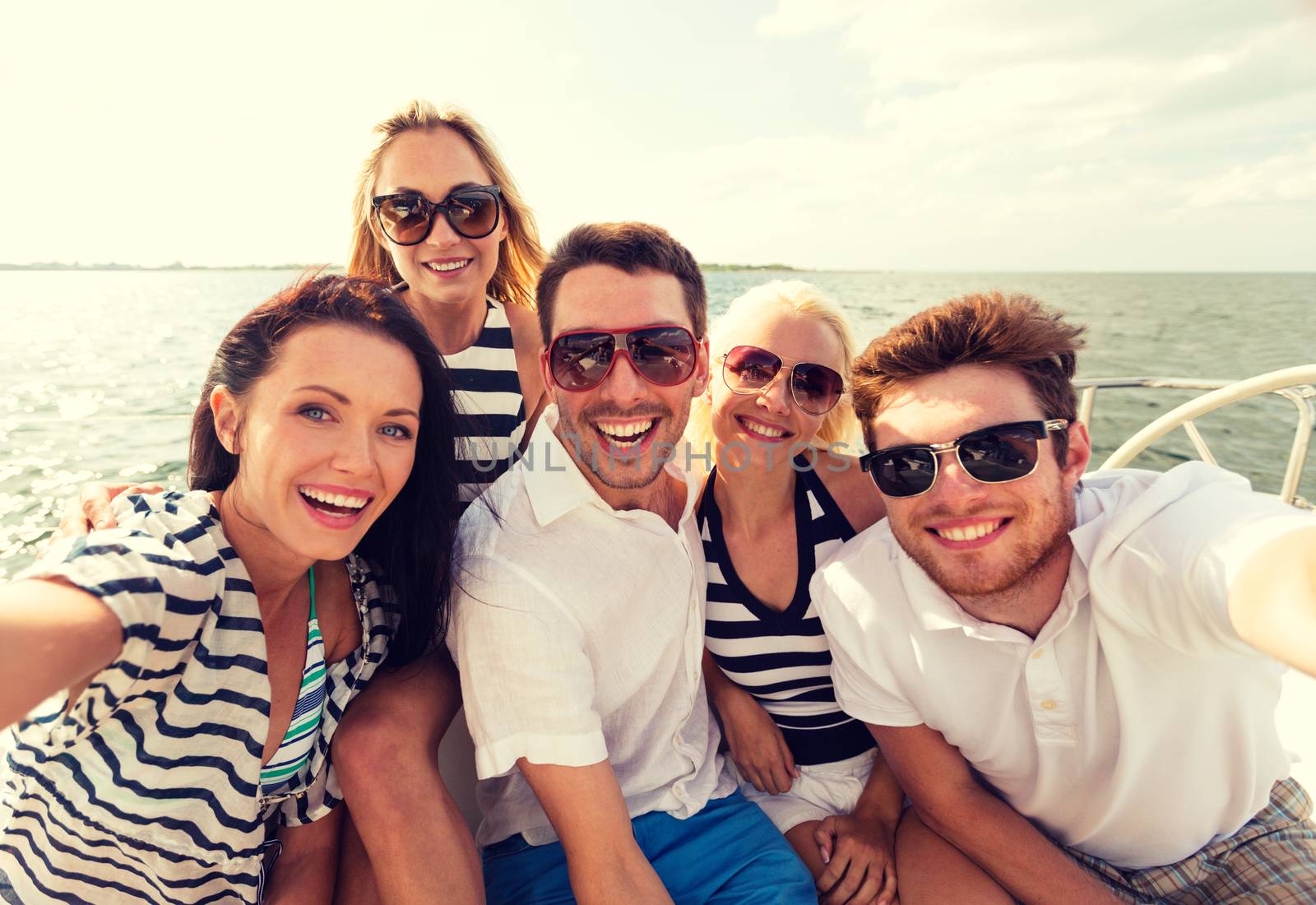 vacation, travel, sea, friendship and people concept - smiling friends sitting on yacht deck and making selfie