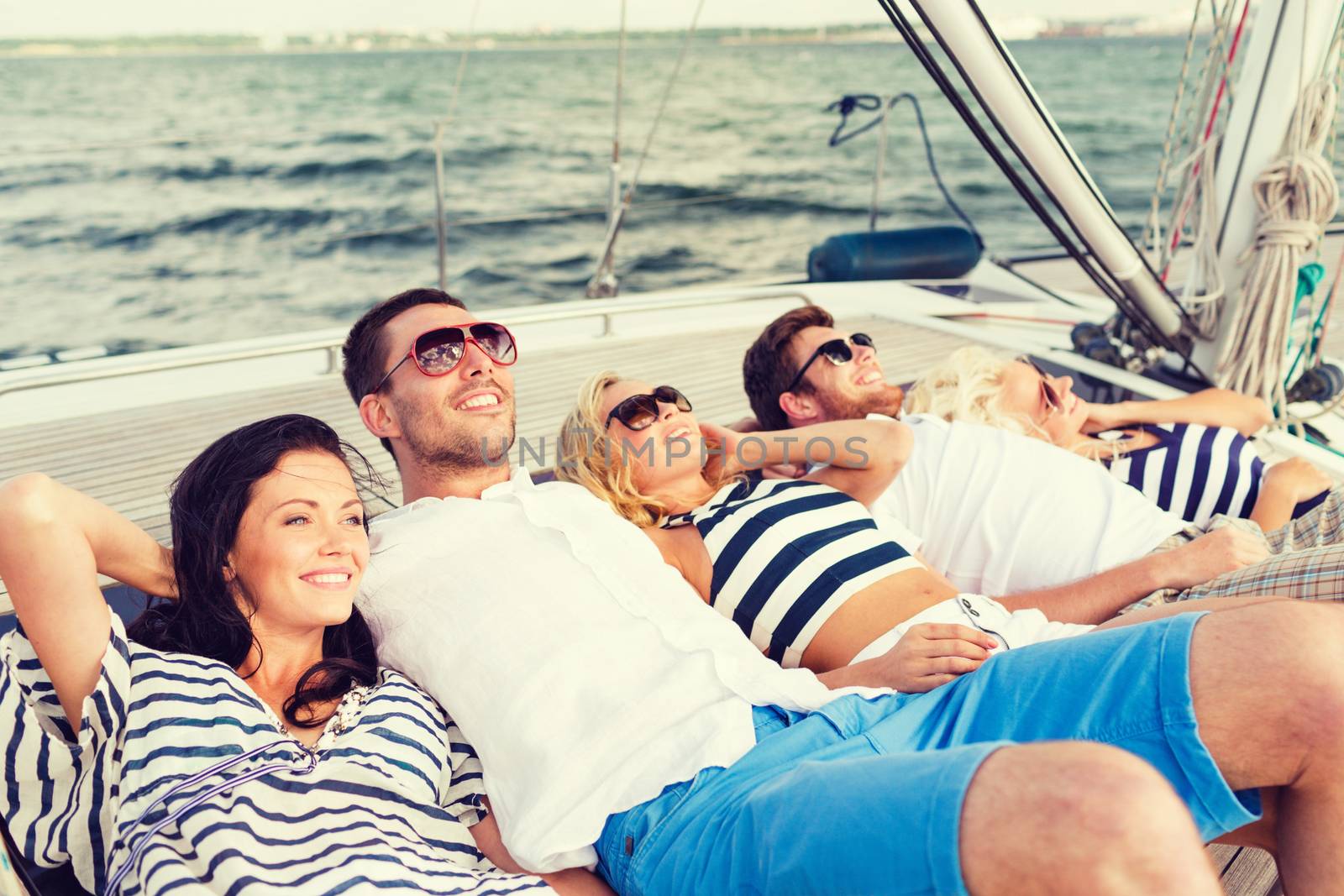 vacation, travel, sea, friendship and people concept - smiling friends lying on yacht deck