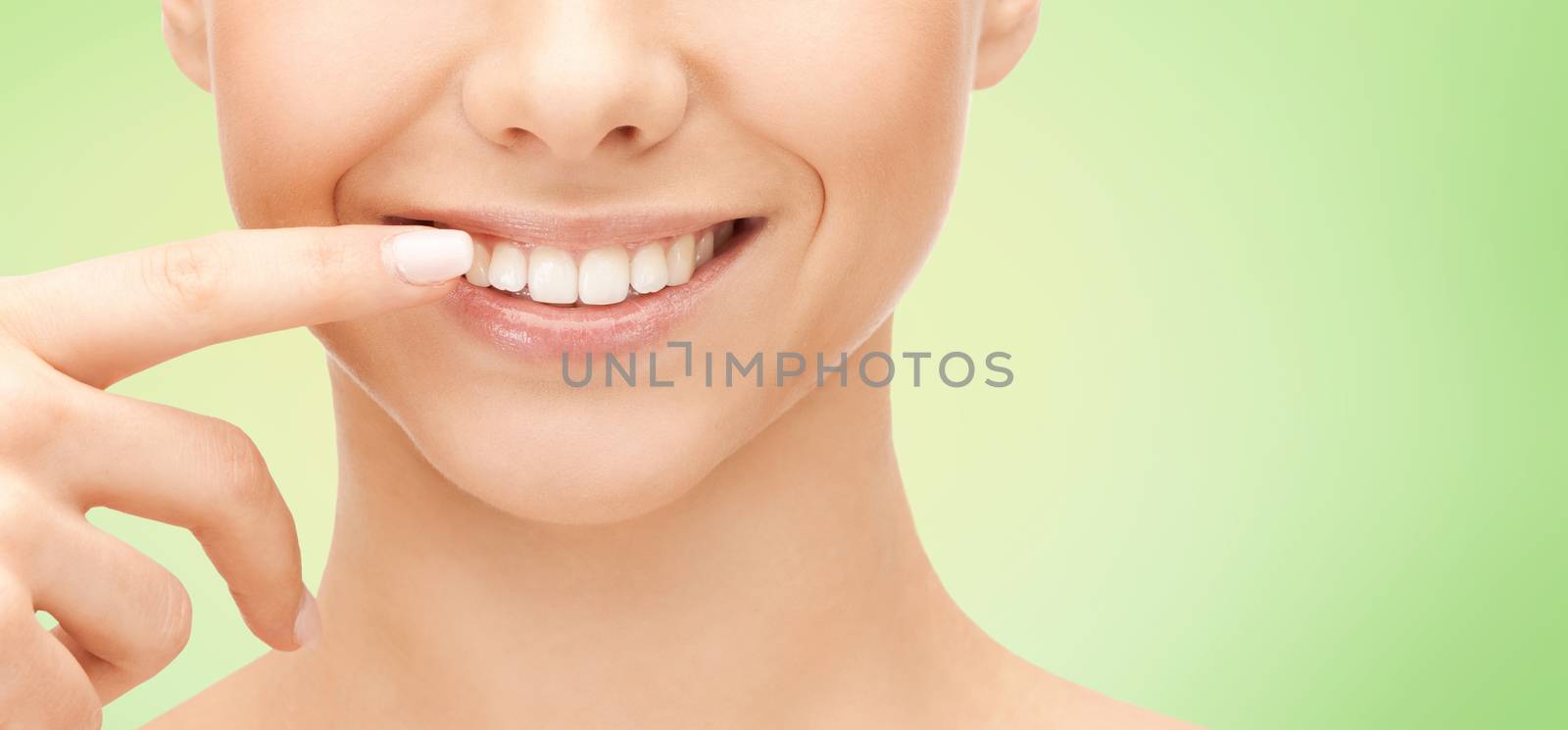 dental health, beauty, hygiene and people concept - close up of smiling woman face pointing to teeth over green natural background