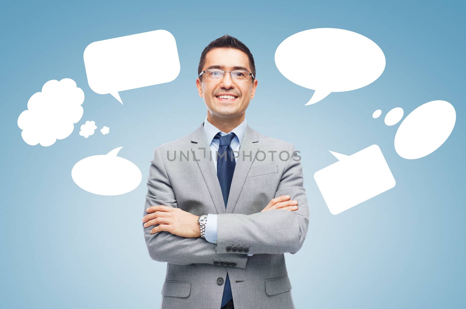 business, people and communication concept - happy smiling businessman in eyeglasses and suit over blue background with text bubbles