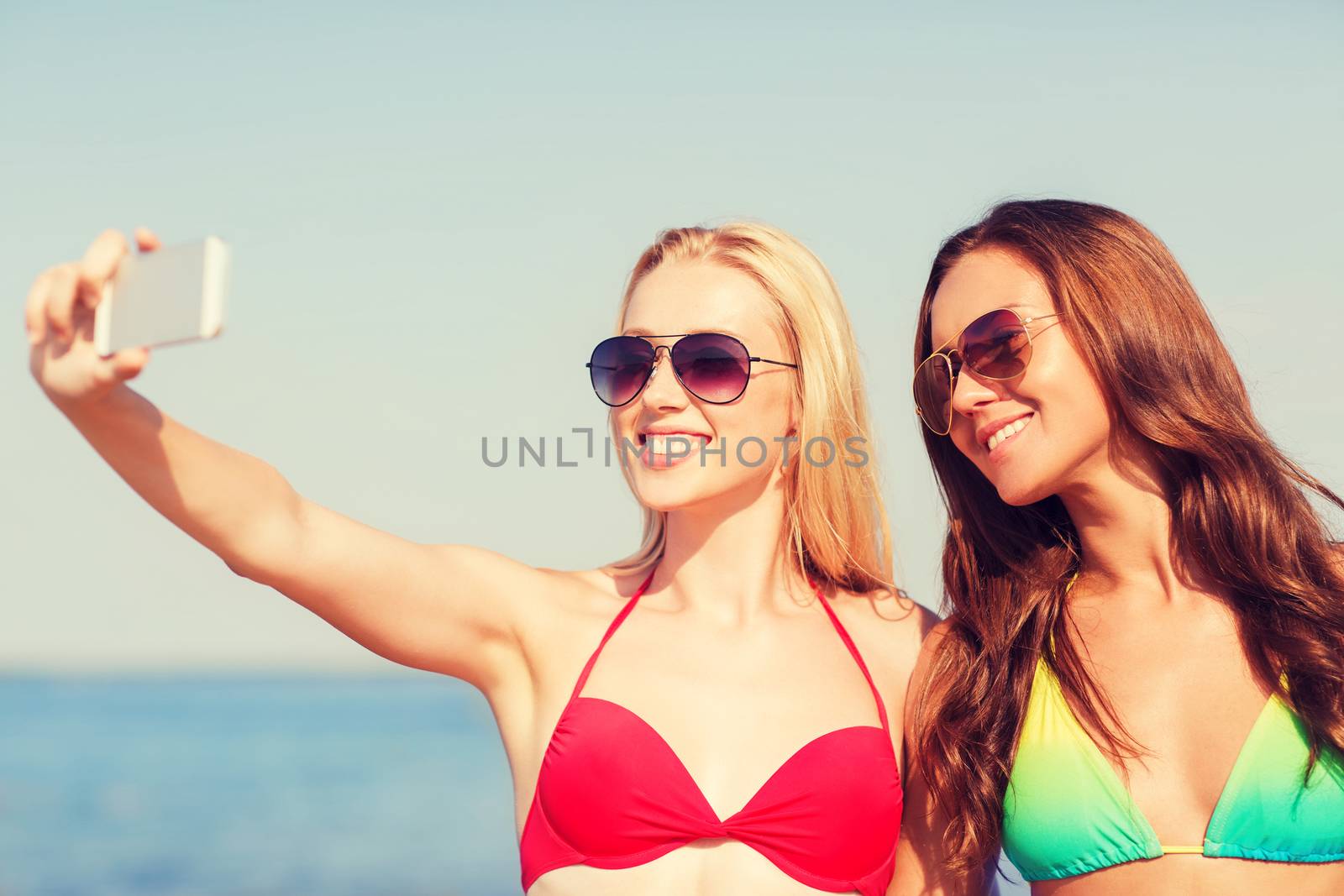 two smiling women making selfie on beach by dolgachov