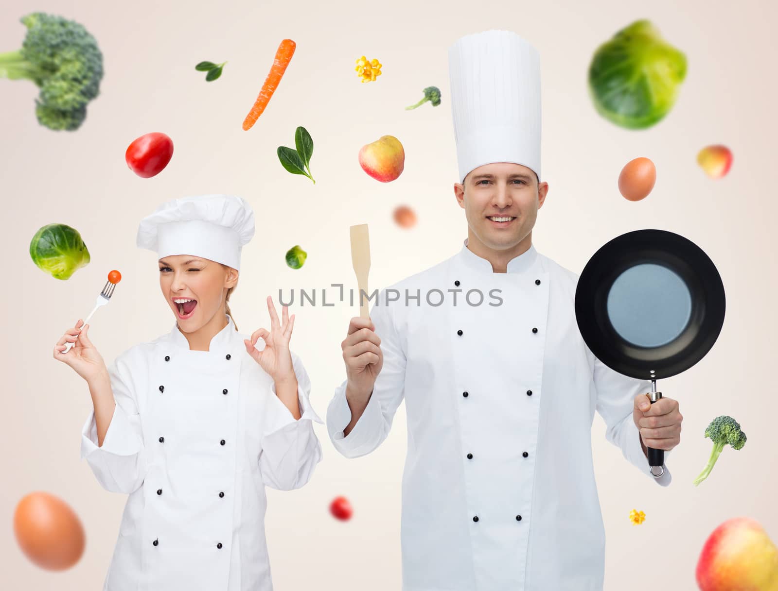 cooking, profession, vegetarian diet and people concept - happy male chef cook holding frying pan and spatula over beige background with falling vegetables