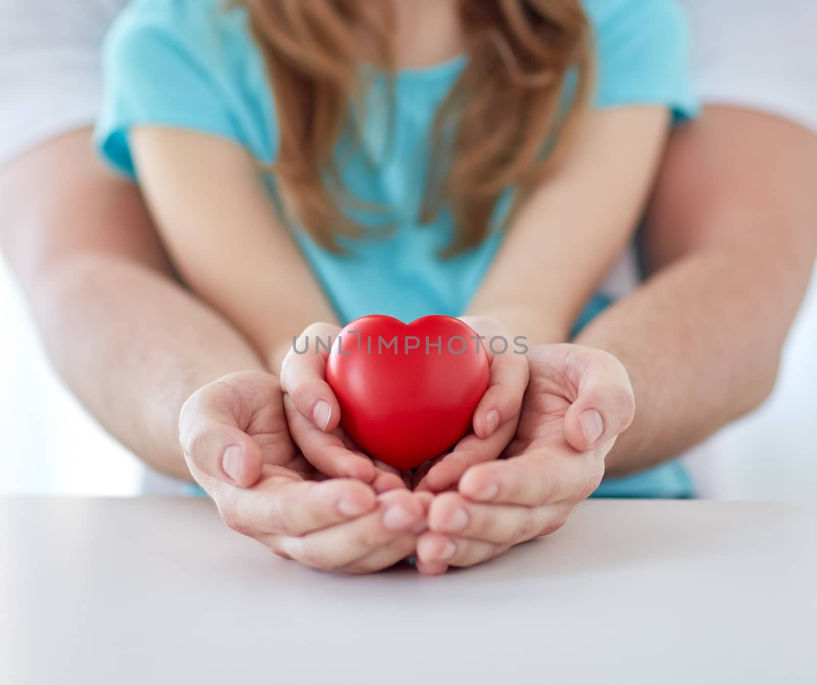 people, charity, family and advertisement concept - close up of father and girl holding red heart shape in cupped hands at home