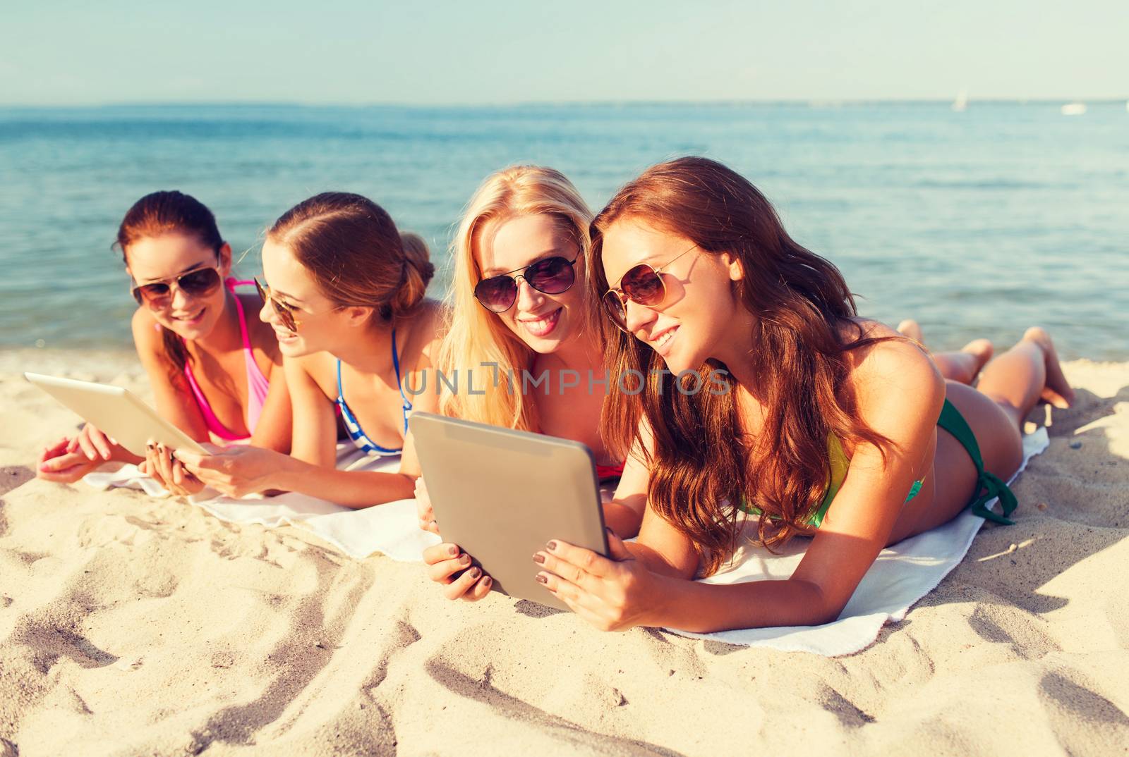 group of smiling young women with tablets on beach by dolgachov