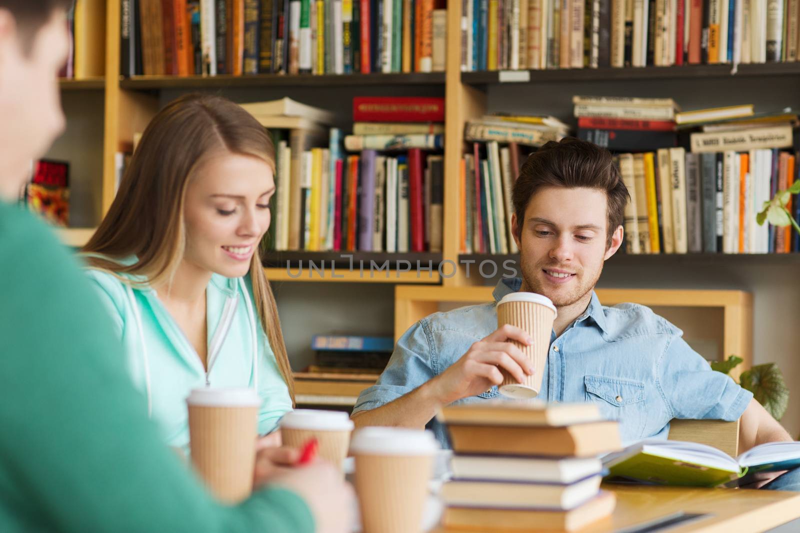 people, knowledge, education and school concept - group of happy students reading books, drinking coffee and preparing to exam in library