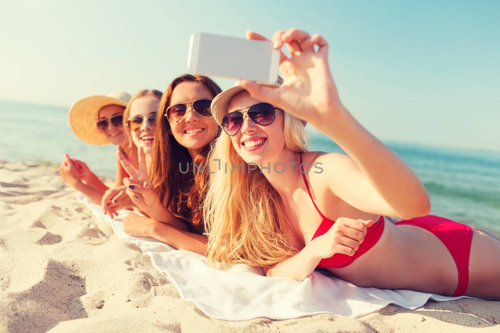 group of smiling women with smartphone on beach by dolgachov