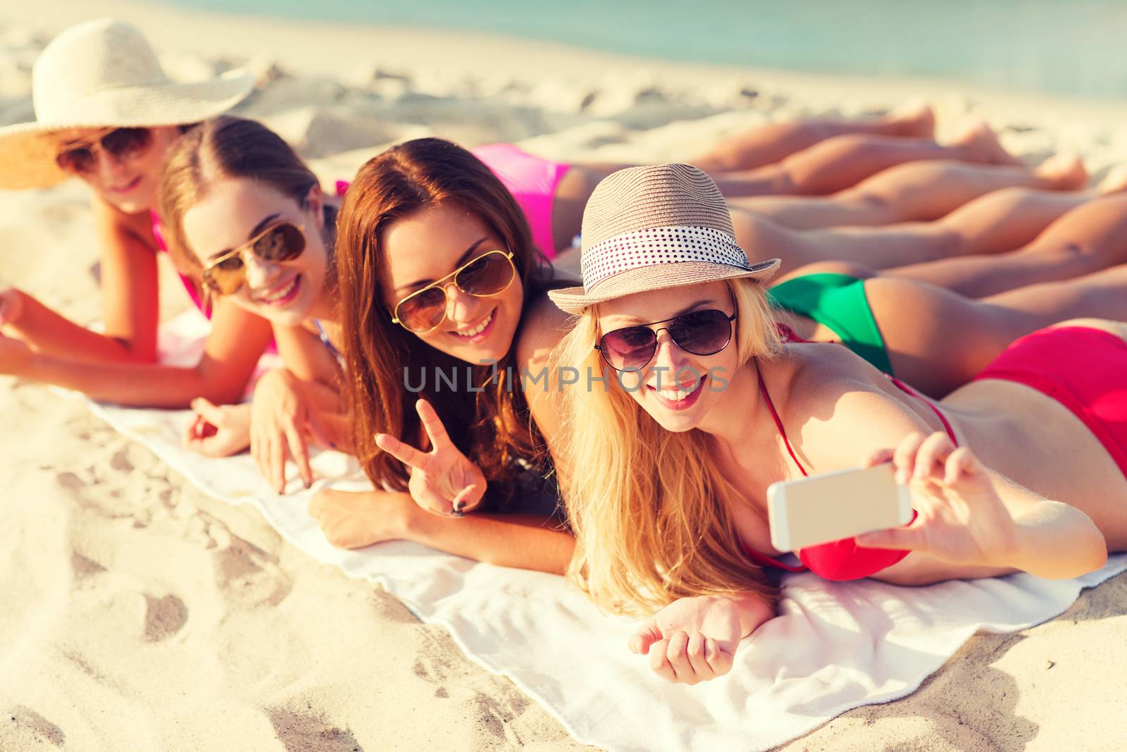 group of smiling women with smartphone on beach by dolgachov