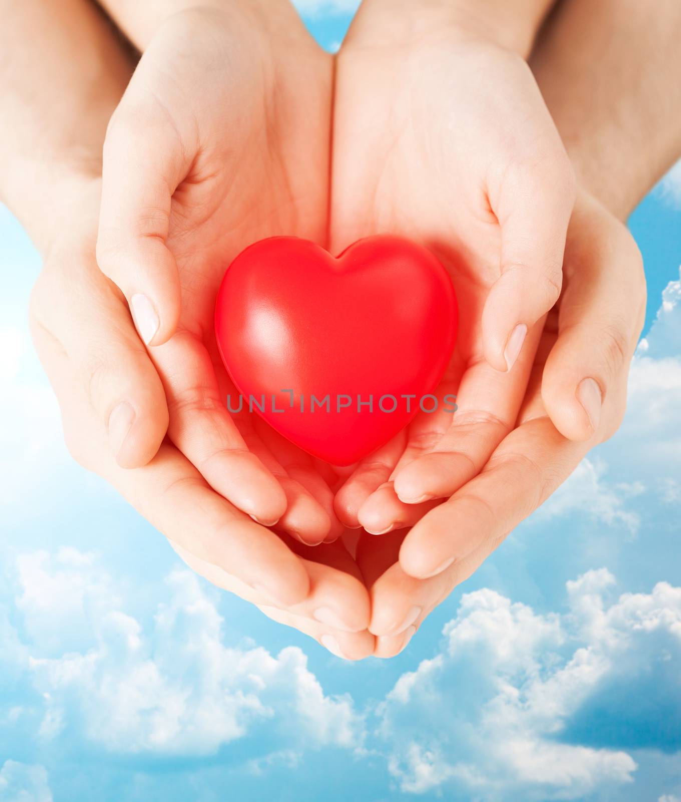 health, love and relationships concept - close up of couple hands with big red heart over blue sky and clouds background