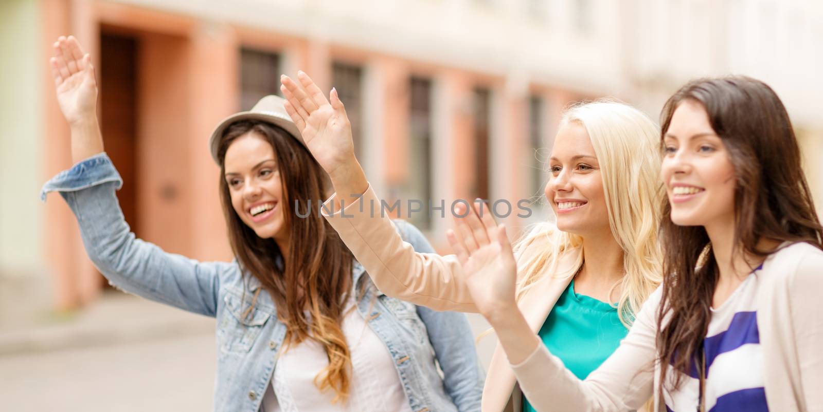 holidays and tourism concept - three beautiful girls waving hands in the city