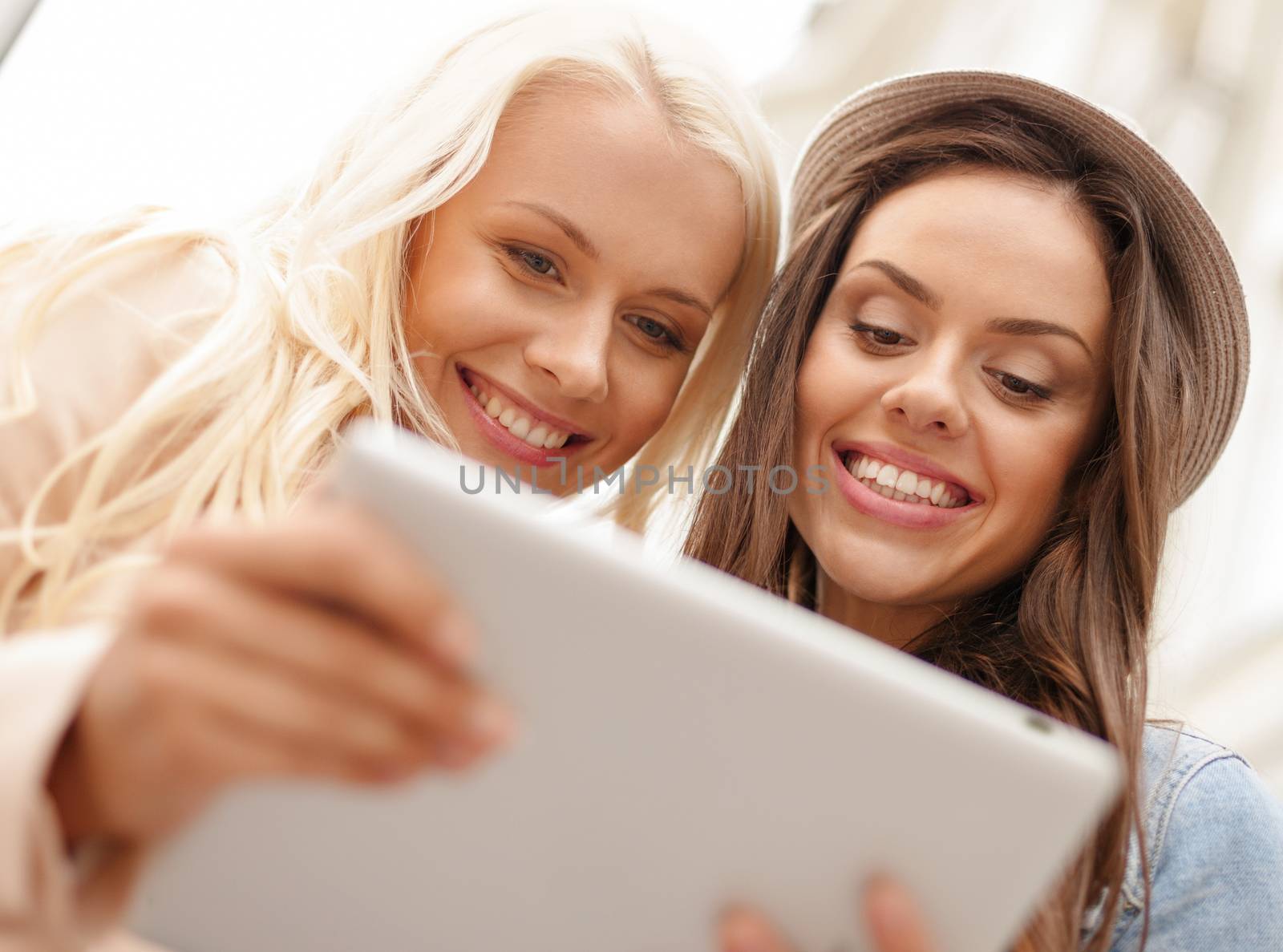 holidays, technology and tourism concept - two beautiful girls toursits looking into tablet pc in the city