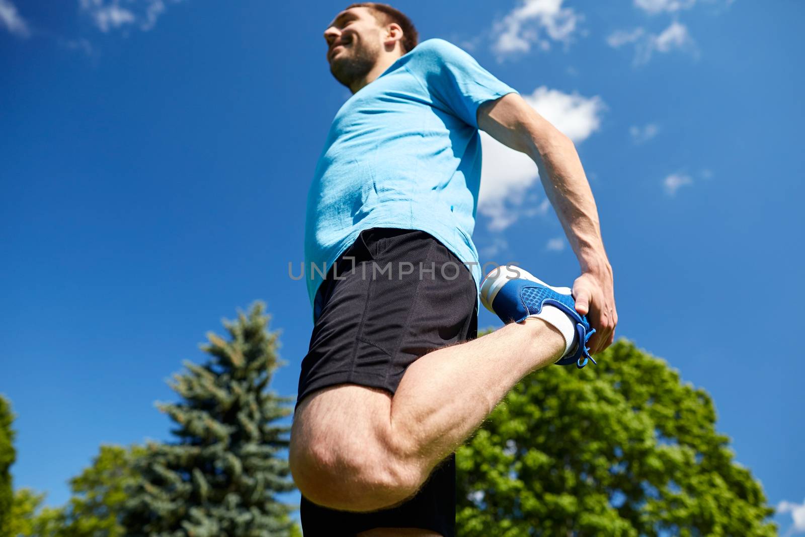 fitness, sport, training, people and lifestyle concept - smiling man stretching leg outdoors