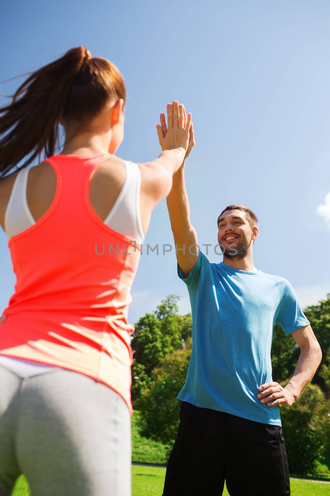 two smiling people making high five outdoors by dolgachov