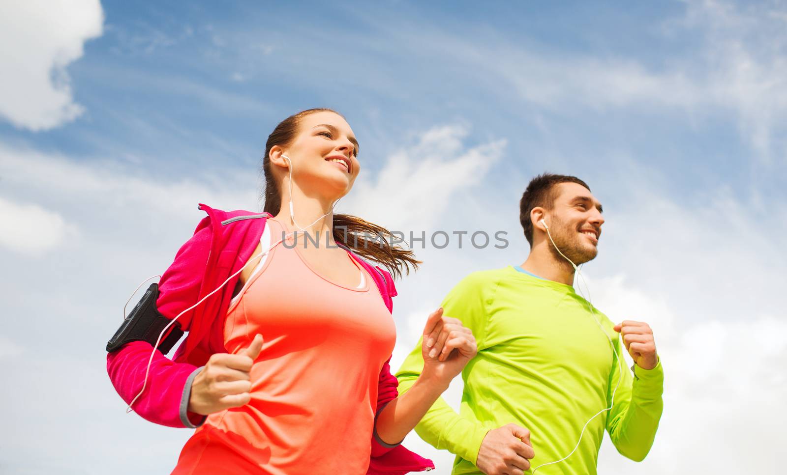 smiling couple with earphones running outdoors by dolgachov