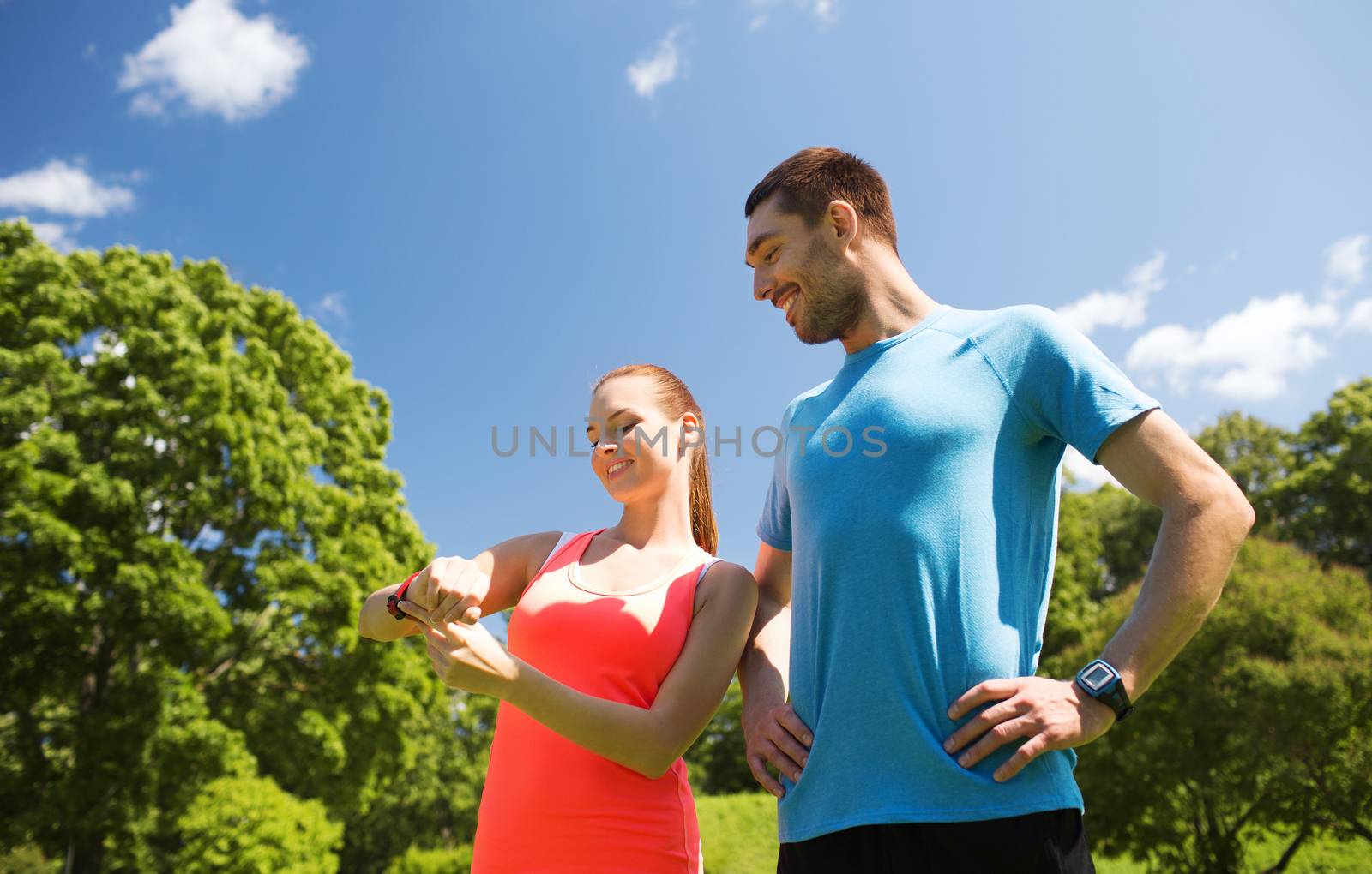 fitness, sport, training, technology and lifestyle concept - two smiling people with heart rate watches outdoors