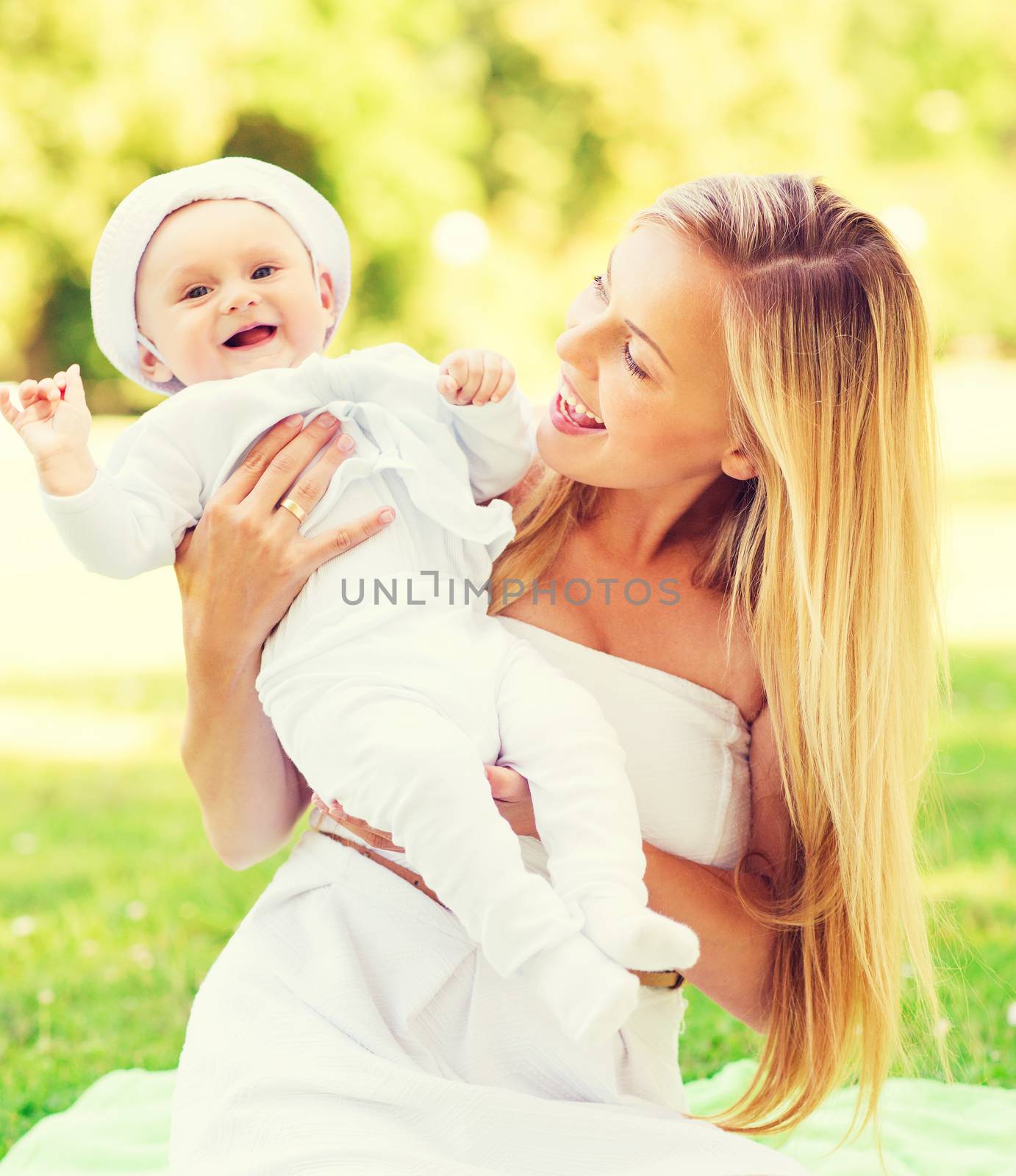 family, child and parenthood concept - happy mother with little baby sitting on blanket in park