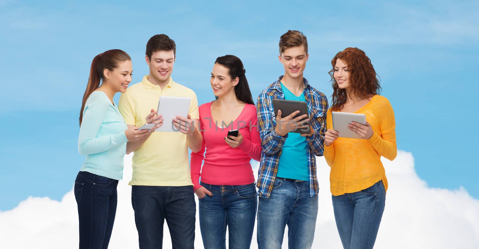 friendship, technolpgy and people concept - group of smiling teenagers with smartphones and tablet pc computers over blue sky with white cloud background