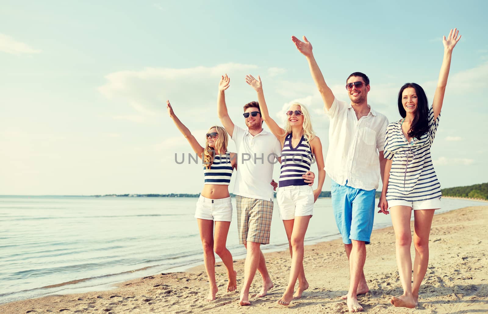 summer, holidays, sea, tourism and people concept - group of smiling friends in sunglasses walking on beach and waving hands