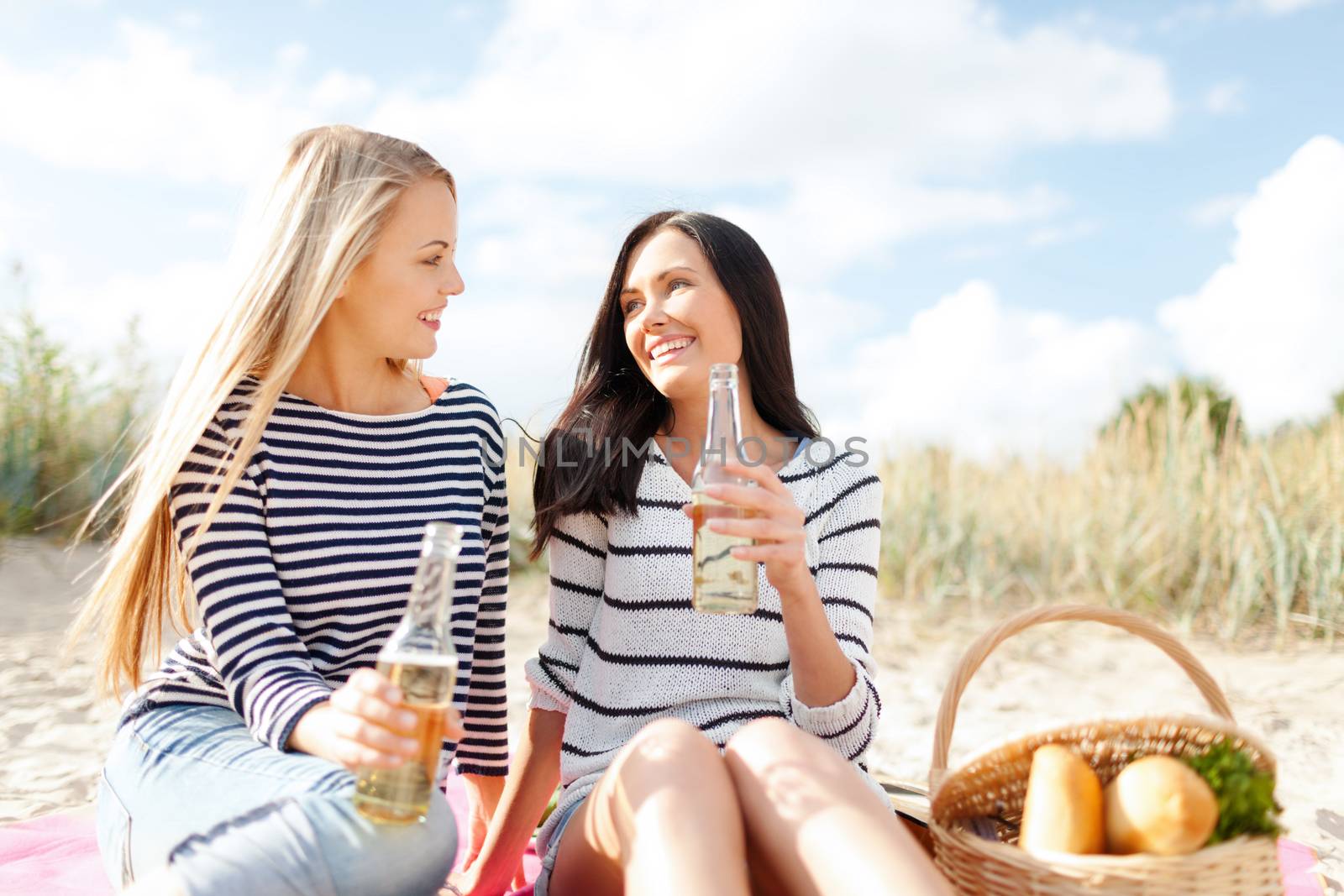 summer holidays, vacation, celebration and people concept - happy teenage girls or young women having picnic and drinking beer or lemonade on beach