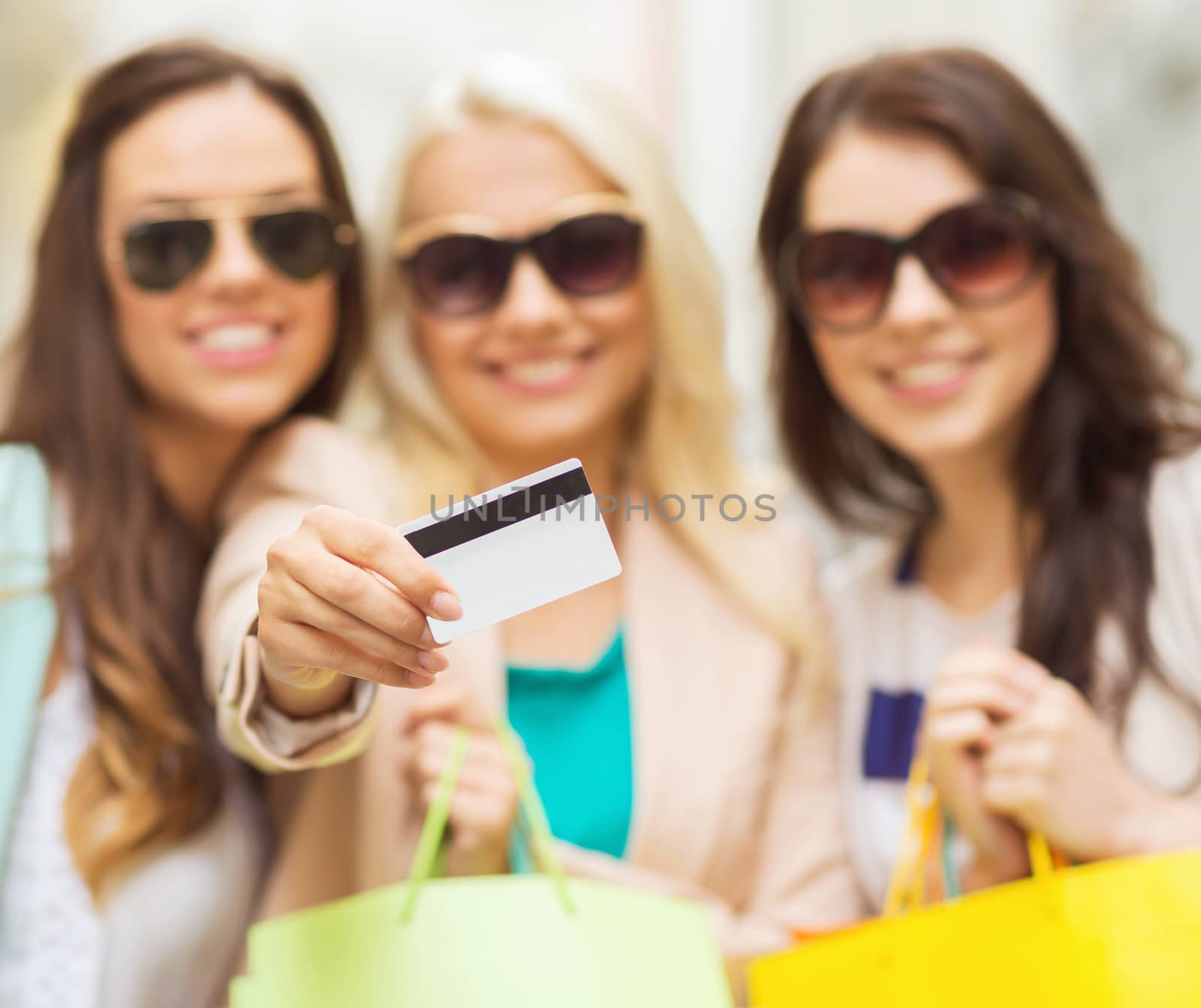 shopping and tourism concept - beautiful girls with shopping bags and credit card in ctiy