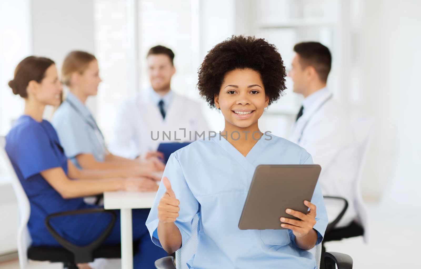 clinic, profession, people and medicine concept - happy female doctor with tablet pc computer over group of medics meeting at hospital showing thumbs up gesture