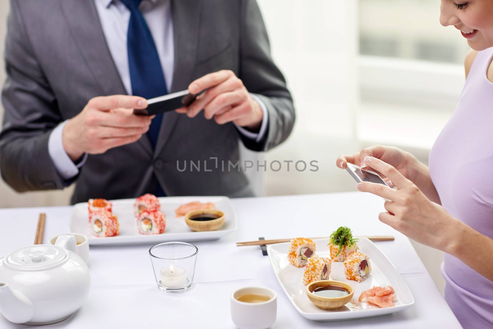 close up of couple with smartphones at restaurant by dolgachov
