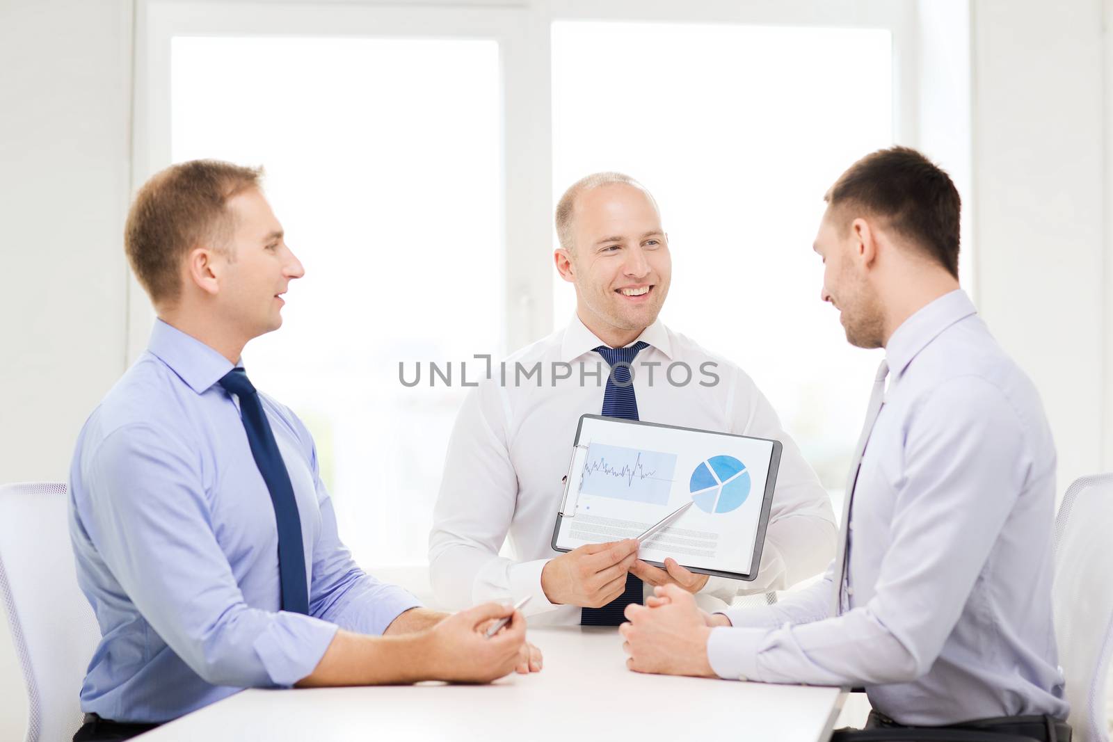 business and office concept - smiling businessman showing others charts in office