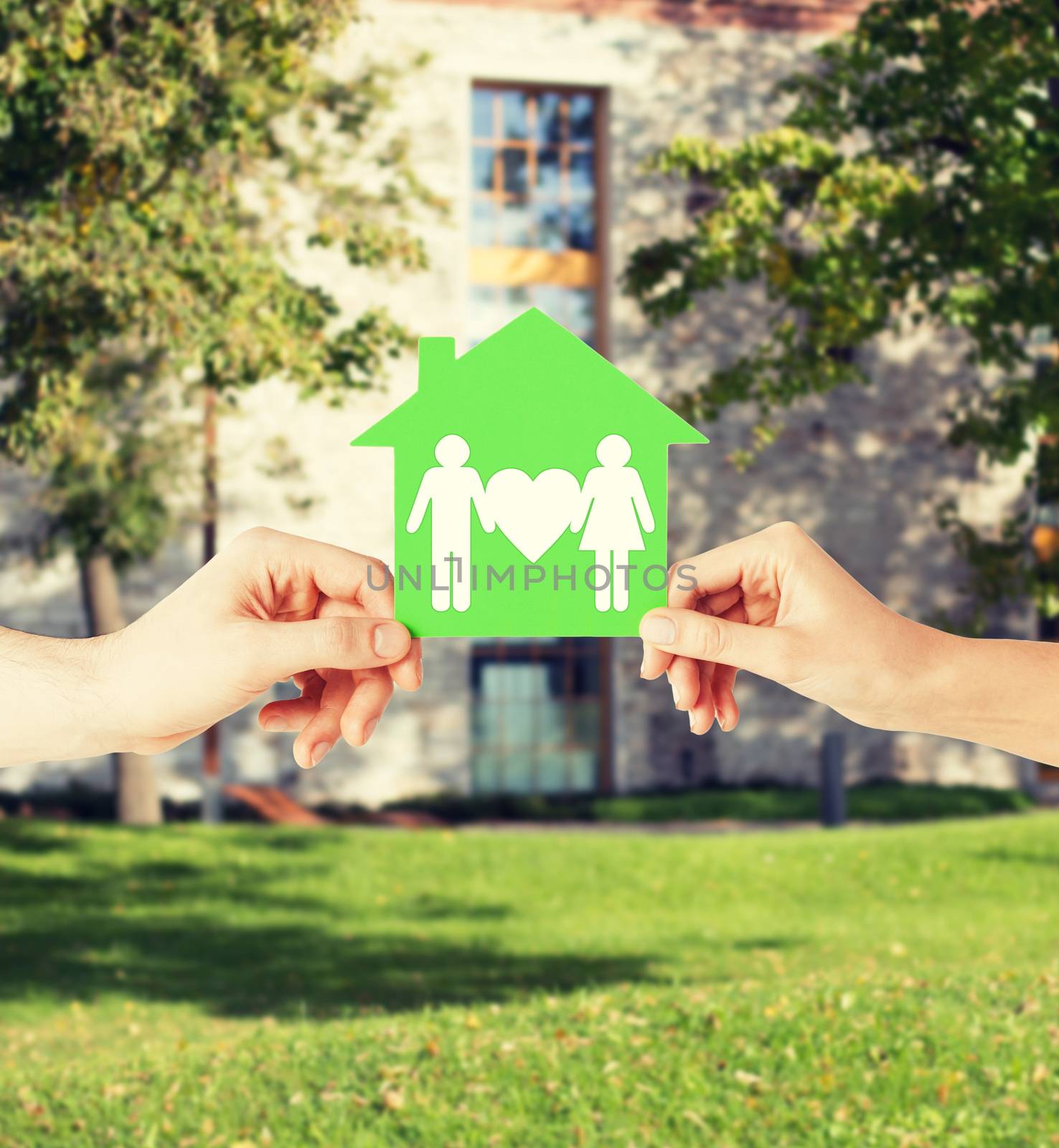 real estate and family home concept - isolated picture of male and female hands holding green paper house with family