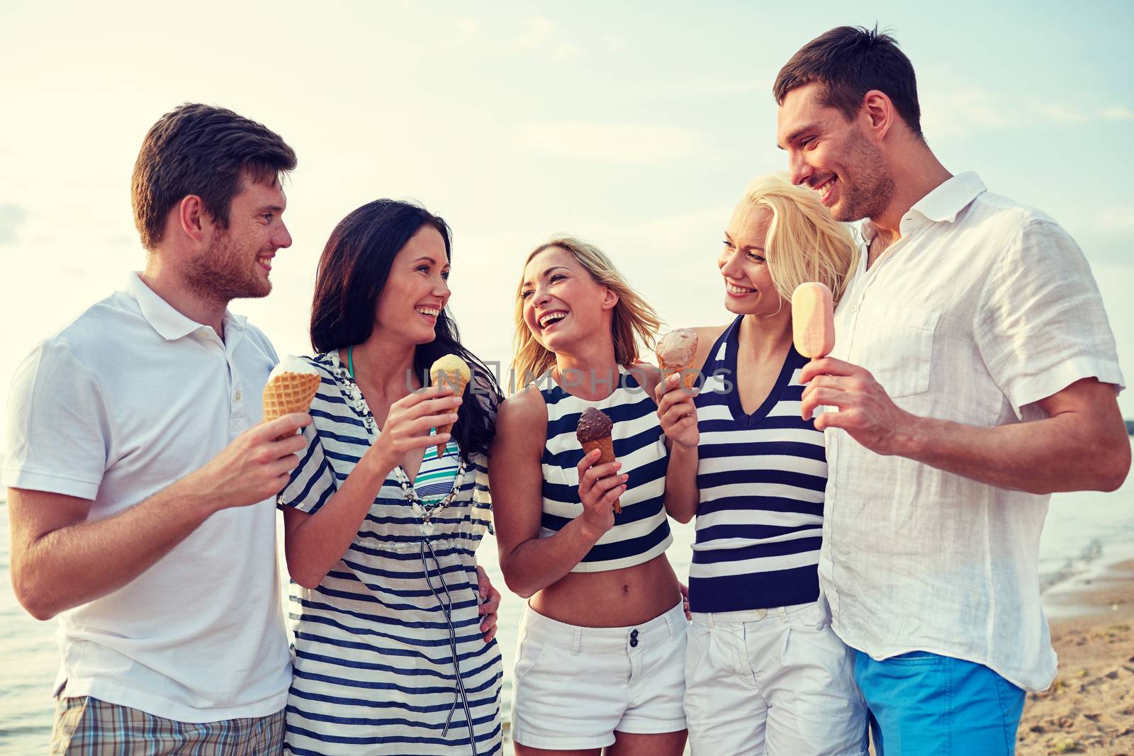 friends eating ice cream and talking on beach by dolgachov