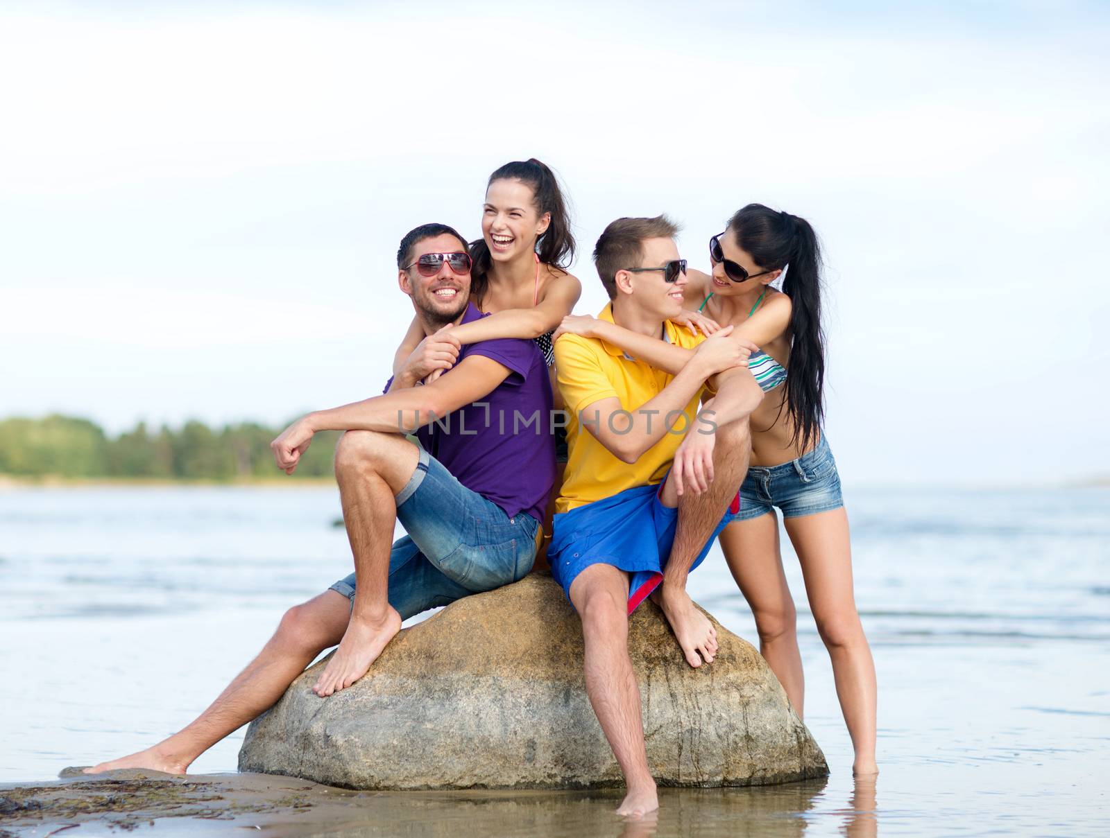 friendship, sea, summer holidays, beach and people concept - group of happy friends sitting on rock