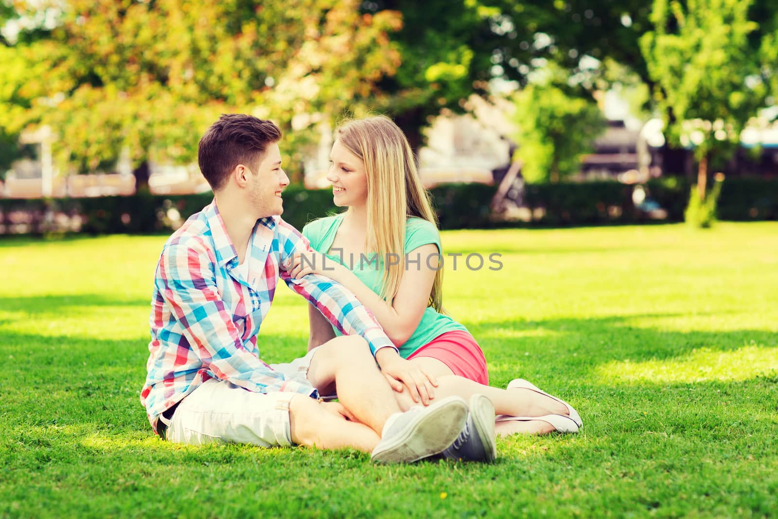 holidays, vacation, love and friendship concept - smiling couple sitting on grass and talking in park