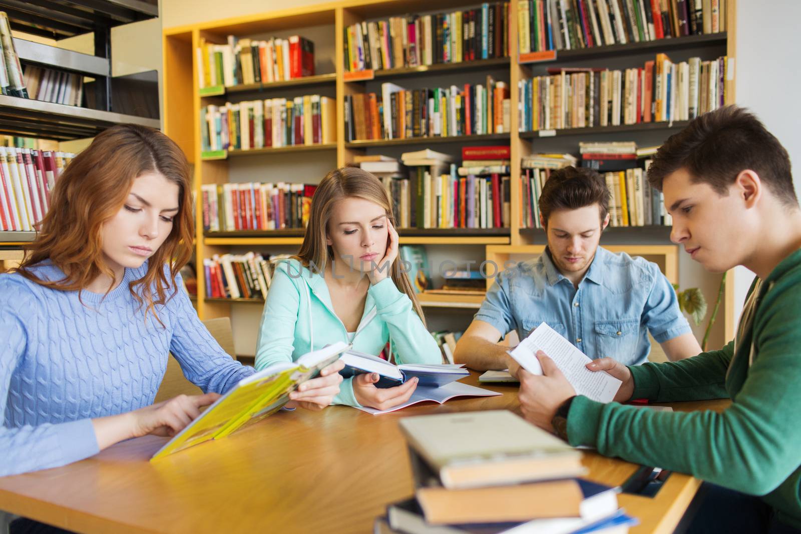 people, knowledge, education, literature and school concept - students reading books and preparing to exams in library