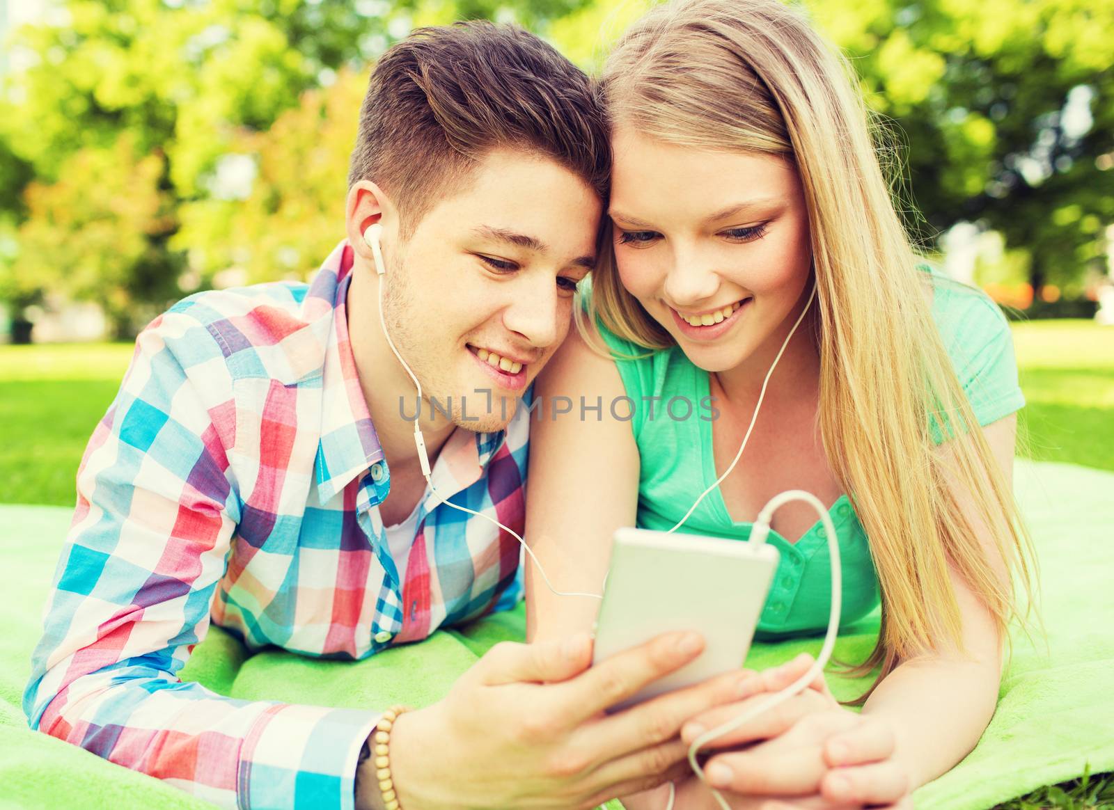 vacation, holidays, technology and friendship concept - smiling couple lying on blanket and making selfie with smartphone in park