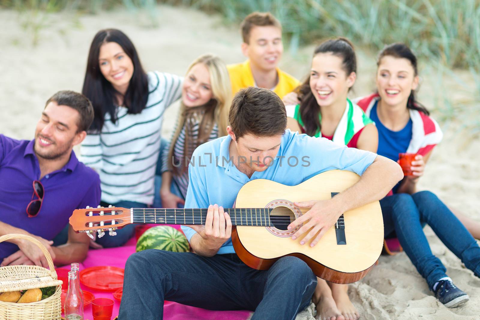 group of happy friends playing guitar on beach by dolgachov