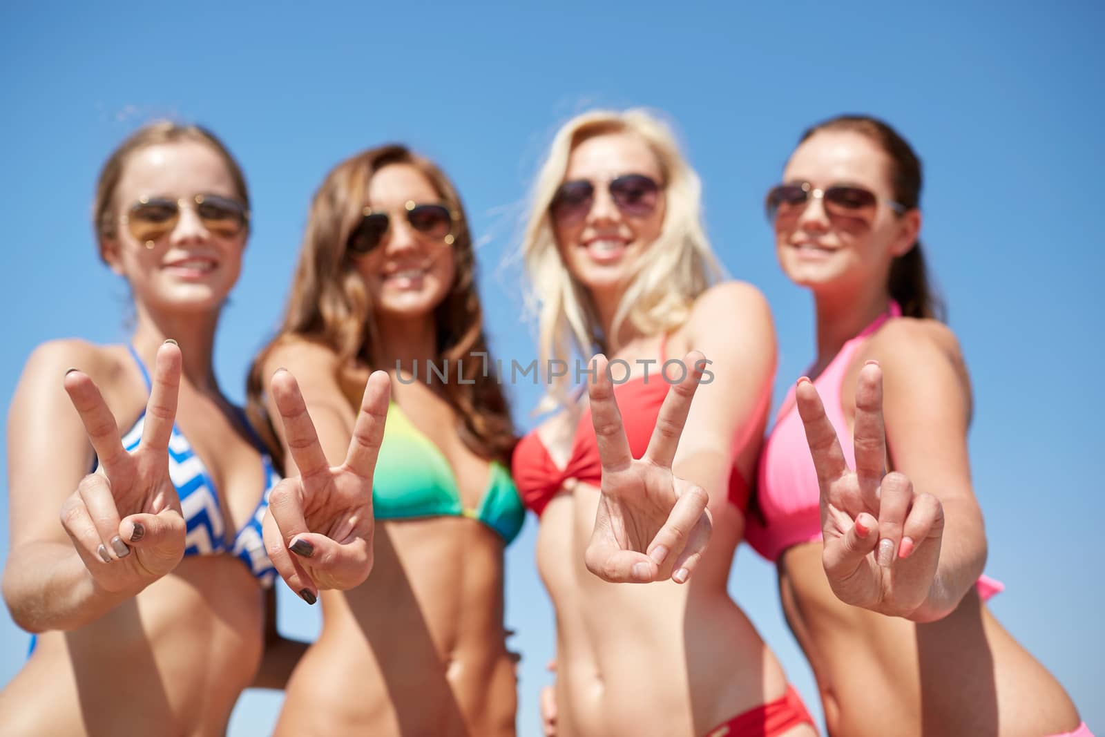 summer vacation, holidays, gesture, travel and people concept - group of smiling young women showing peace or victory sign over blue sky background