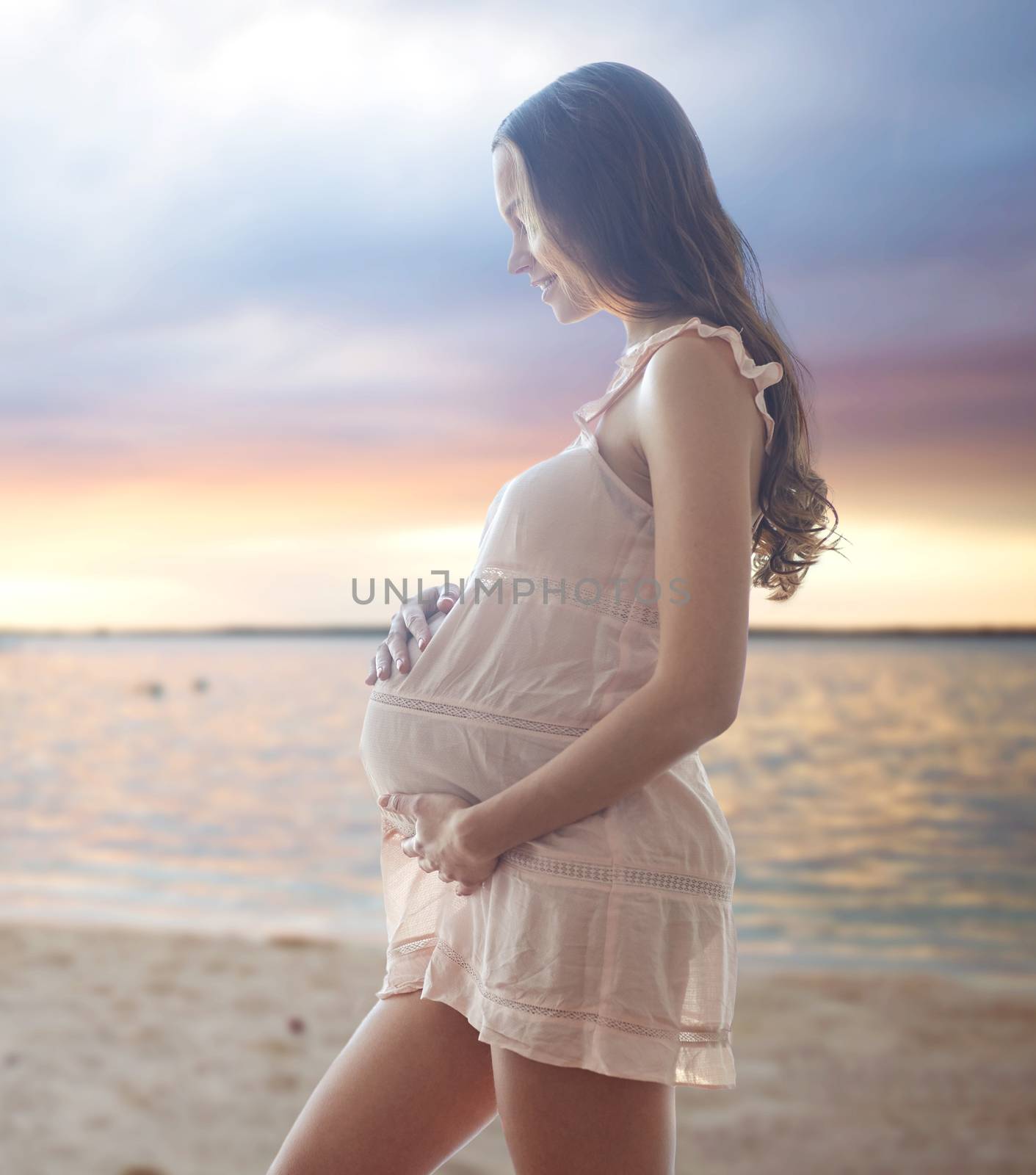 pregnancy, motherhood, people and expectation concept - happy pregnant woman in chemise over sunset on beach background