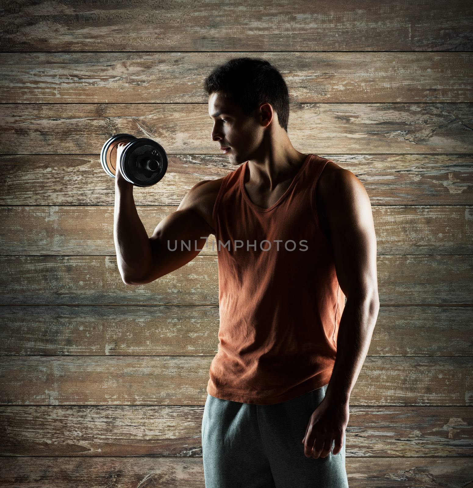 sport, fitness, weightlifting, bodybuilding and people concept - young man with dumbbell flexing biceps over wooden wall background