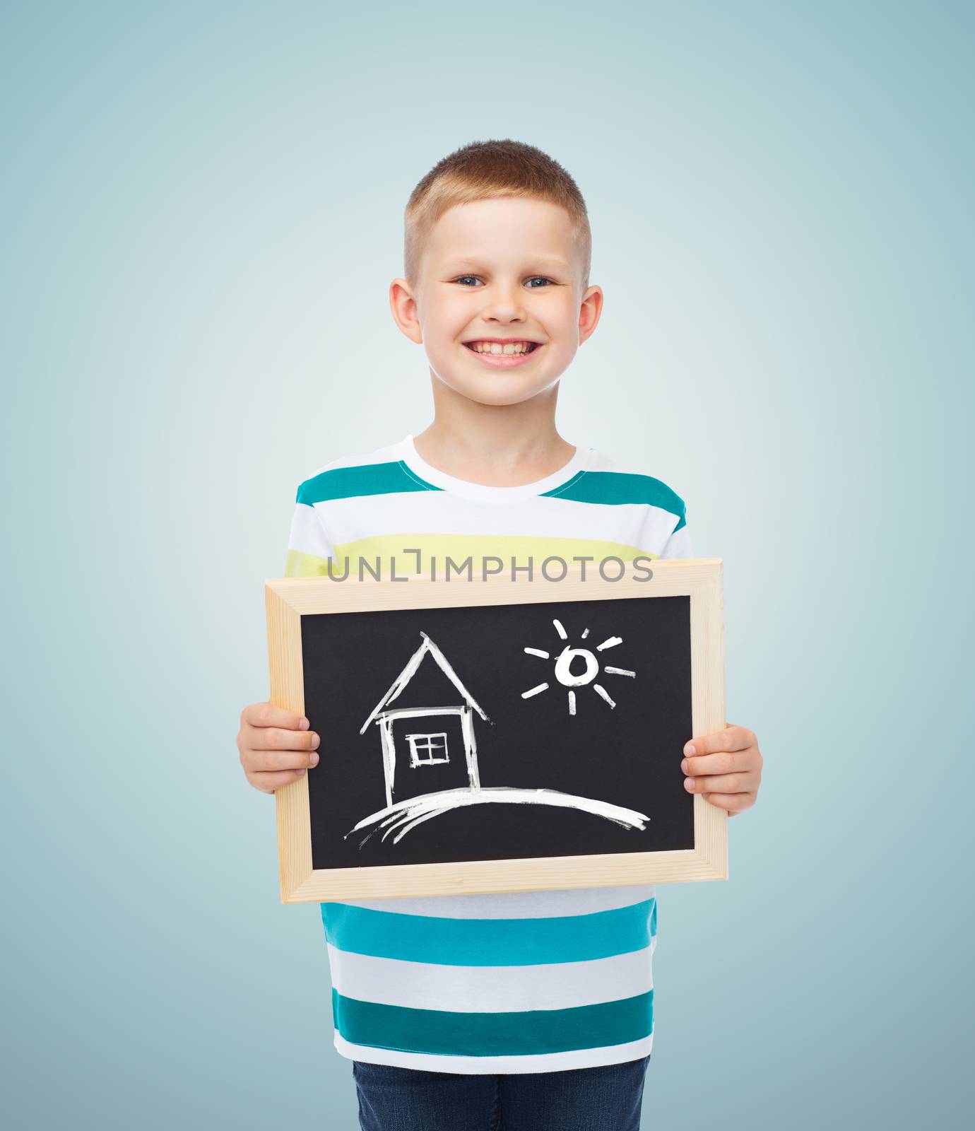 education, creativity, drawing and children concept - smiling little boy holding black chalk board with picture of home over blue background