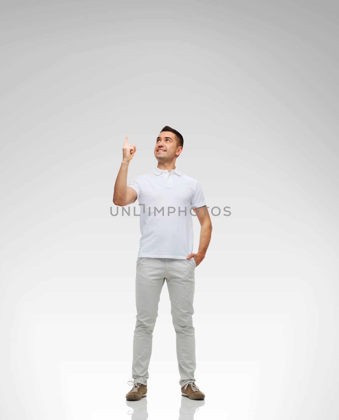 happiness, gesture and people concept - smiling man pointing finger up over gray background
