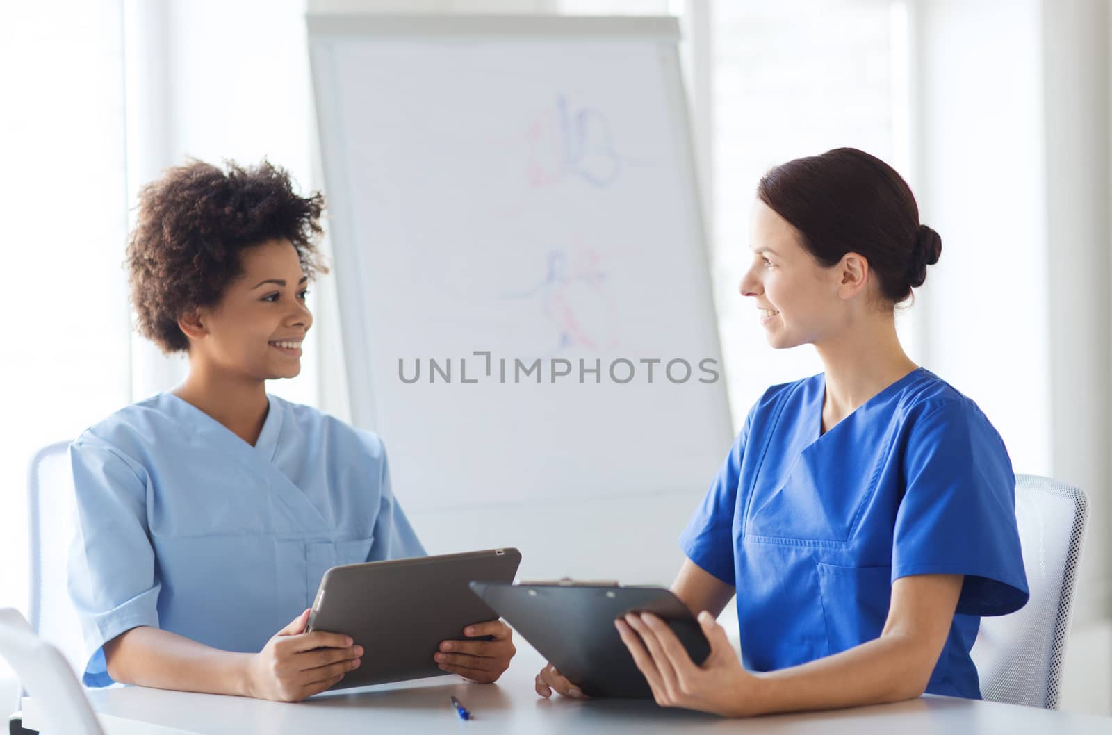 hospital, profession, people and medicine concept - group of happy doctors with tablet pc computer and clipboard meeting at medical office